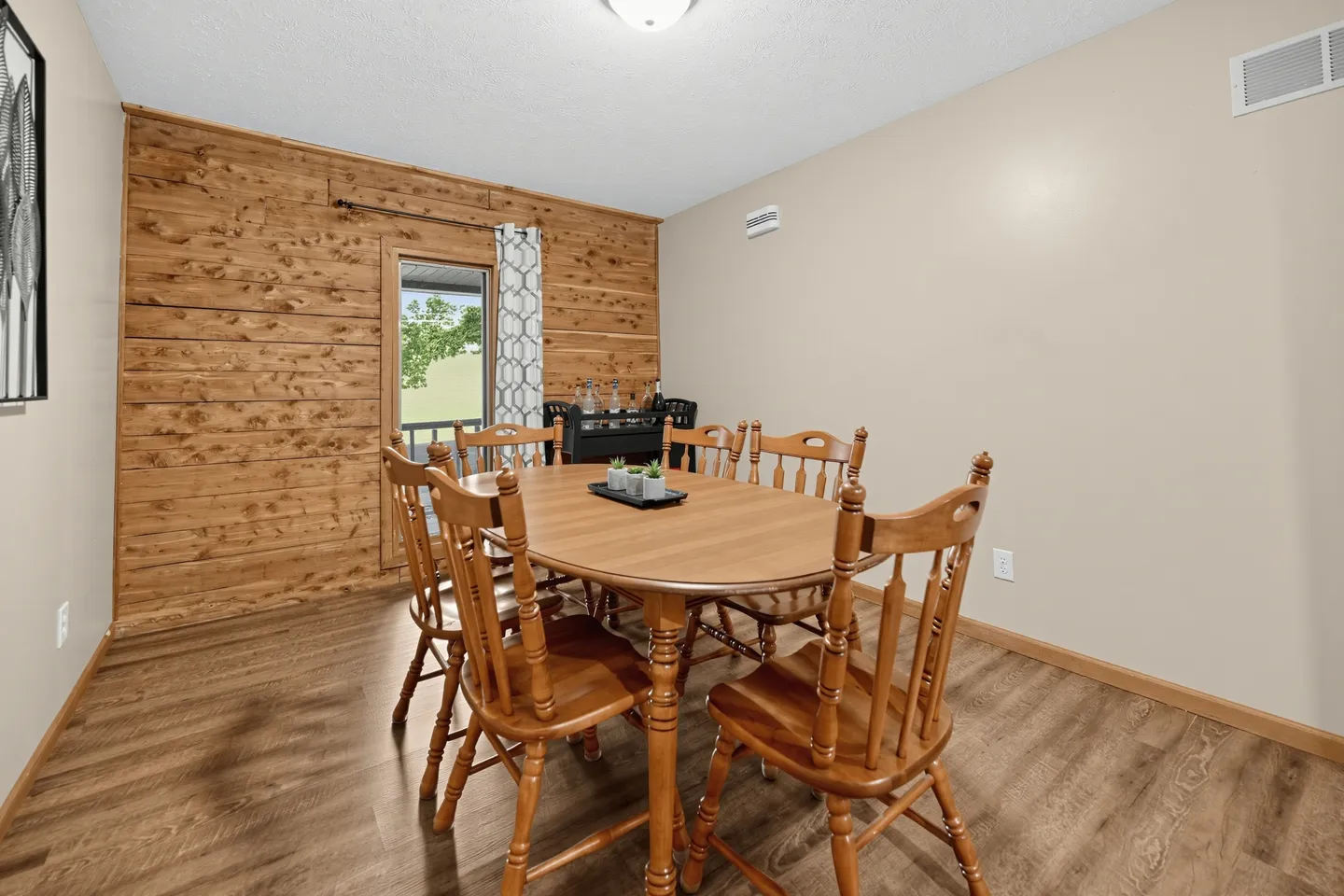 Dining room with an oval wooden table, spindle-back chairs, wood-plank accent wall, and wood-look flooring.
