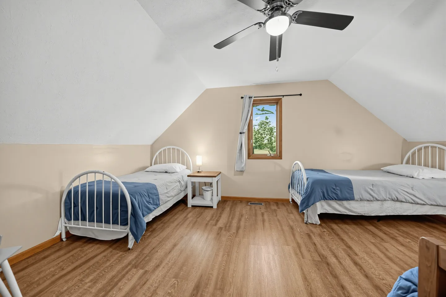 Bedroom with sloped ceilings, two twin beds with white metal frames, wood-look flooring, and a ceiling fan.