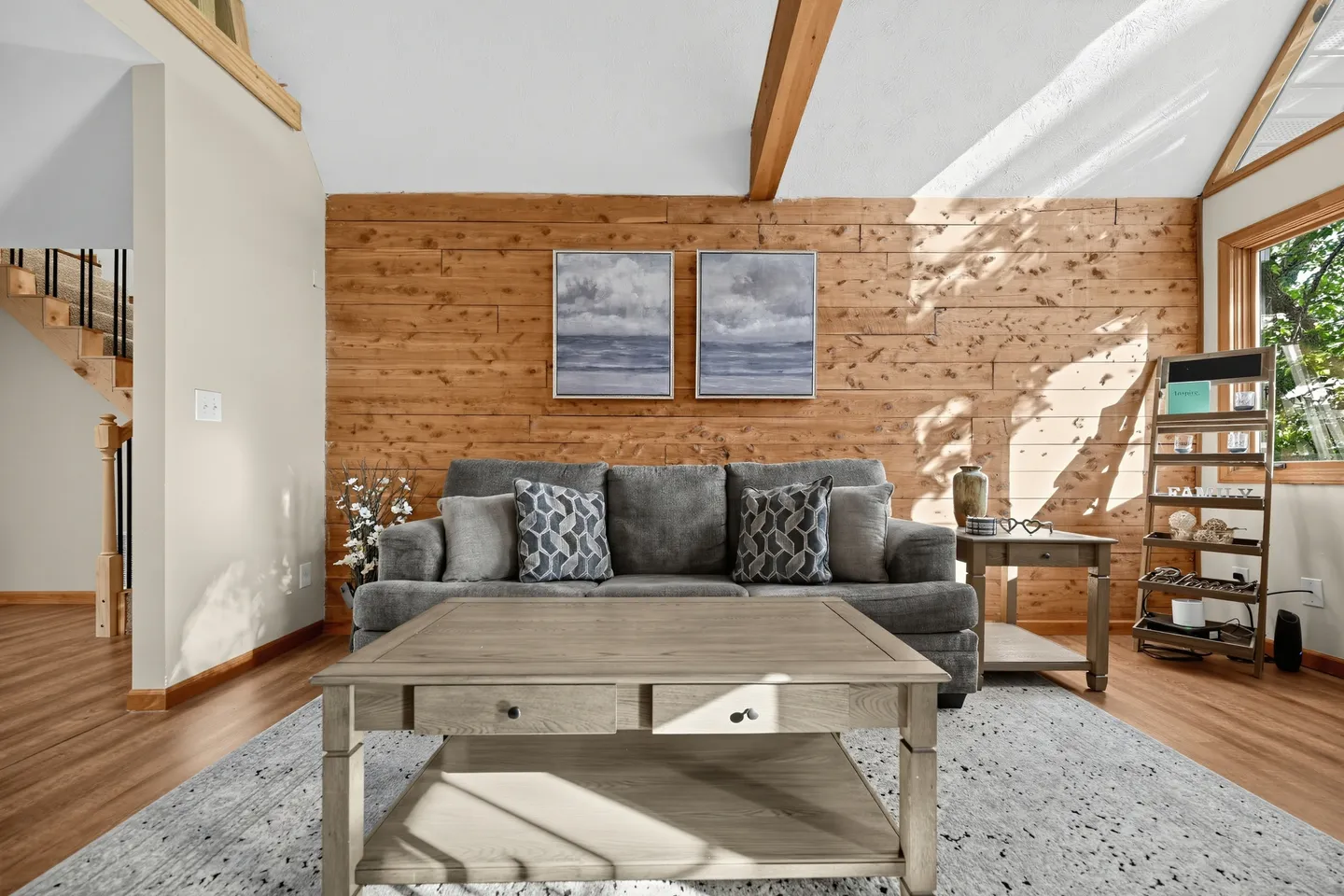Living room featuring a grey couch against a wood-paneled accent wall, a light wood coffee table, and vaulted ceilings with exposed beams.