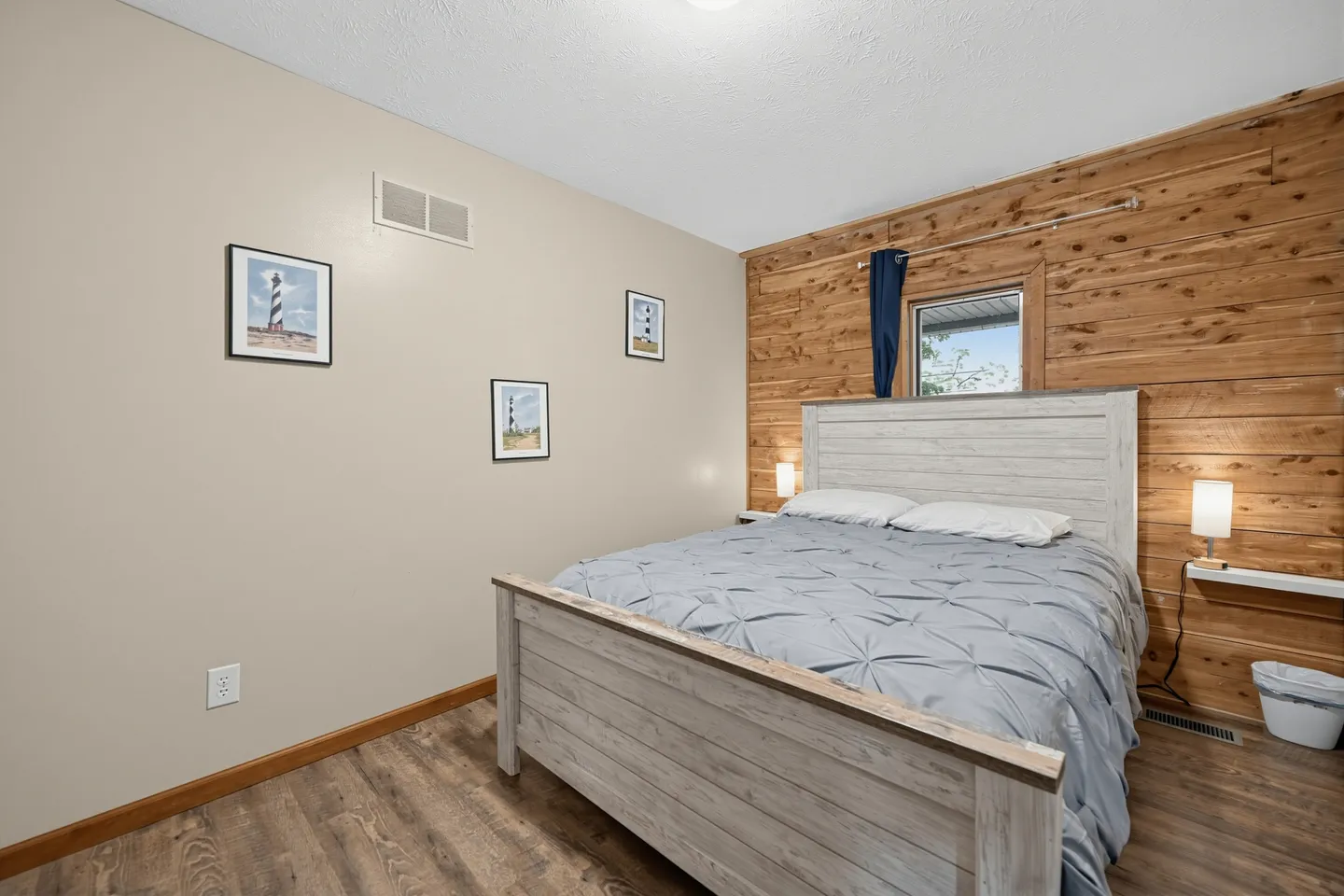 Bedroom featuring a light wood-tone bed frame against a wood-paneled accent wall with a small window.