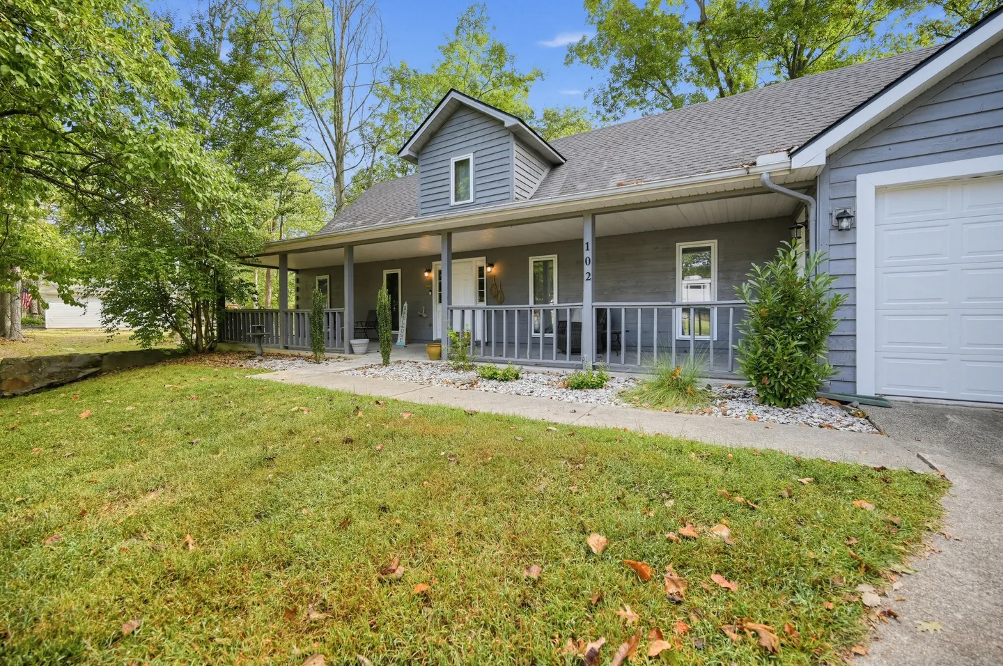 Front view of a gray home with a covered front porch, white garage door, and green lawn with trees.