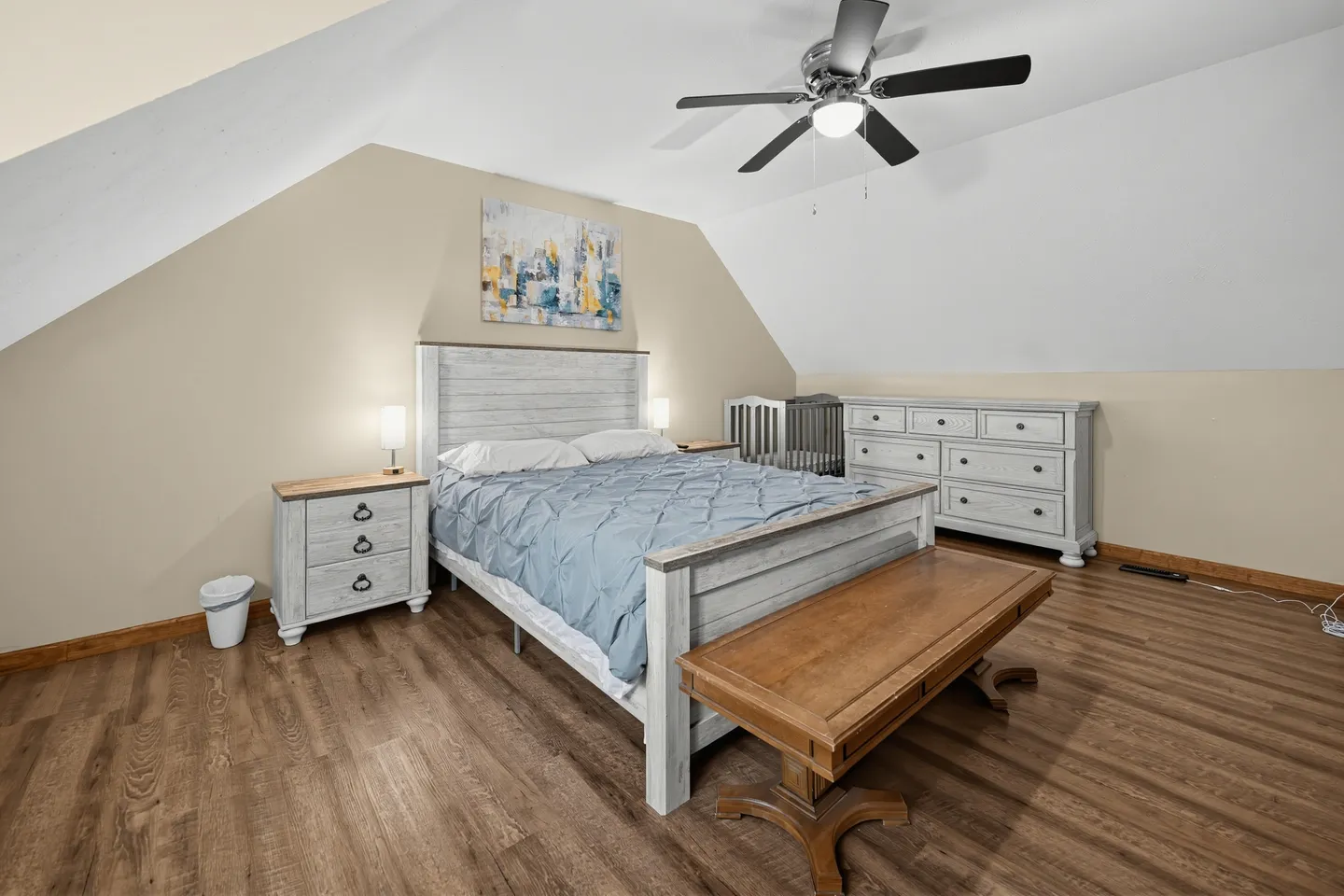Bedroom with sloped ceiling, wood-look floors, a wooden bed, bench, nightstands, and a dresser.