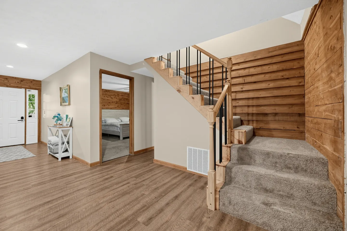Entryway and staircase with carpeted steps, wooden accent walls, wood-look flooring, and a doorway showing a bedroom.