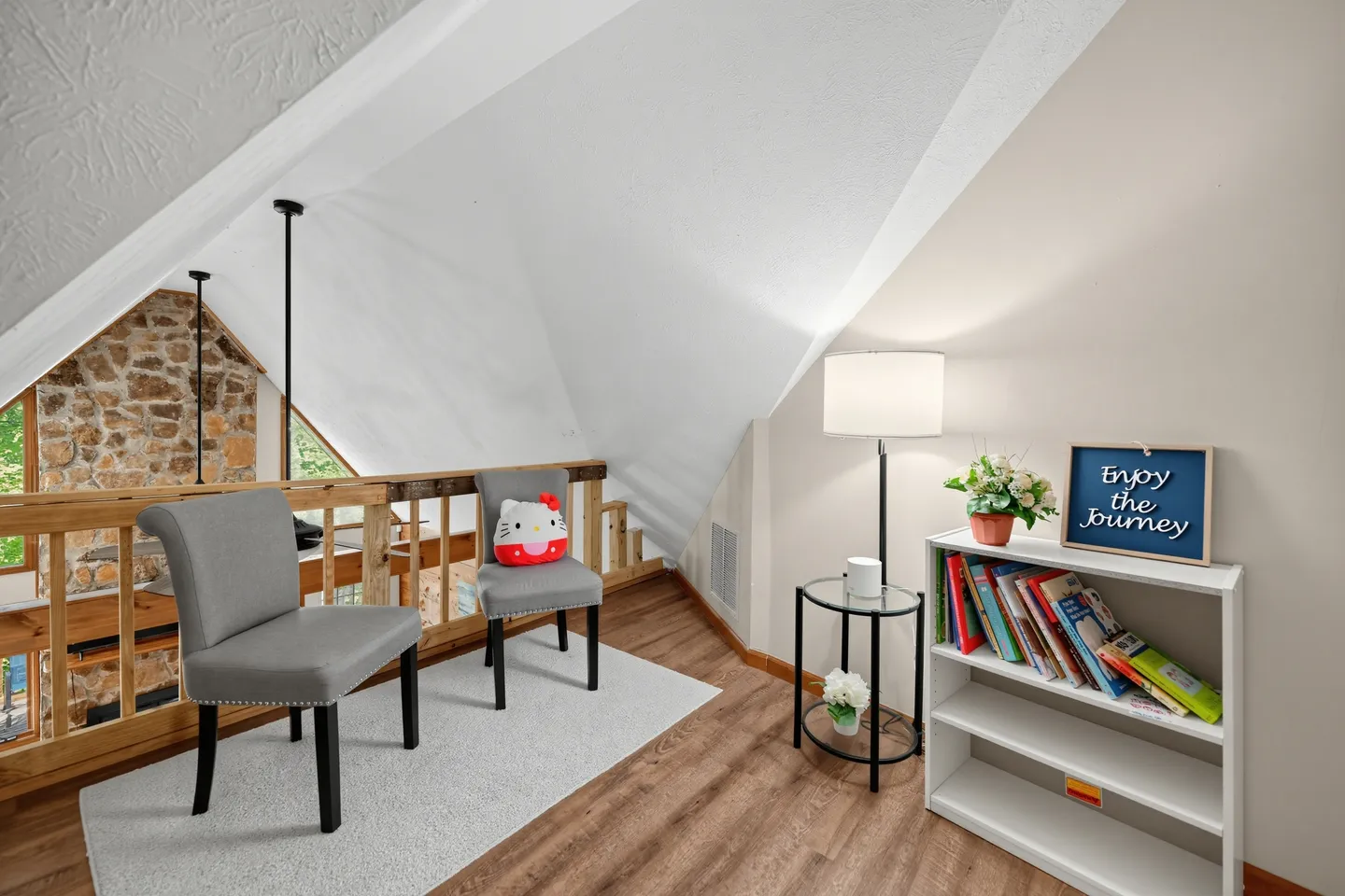 Upstairs loft sitting area with two grey upholstered chairs, a small bookcase, floor lamp, and a wood railing overlooking the lower level.