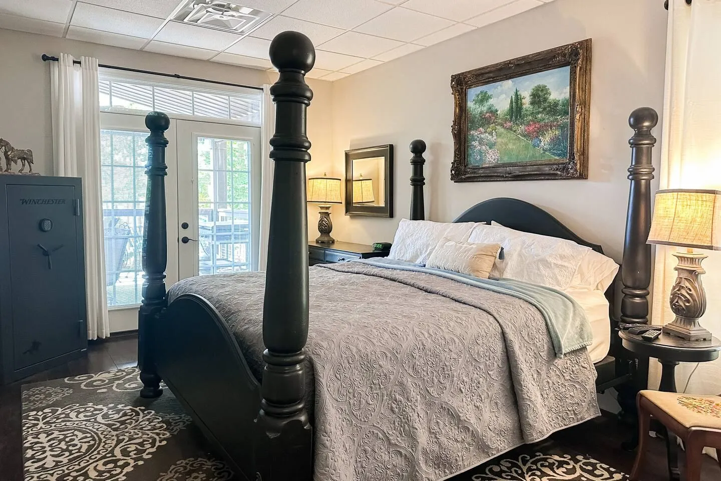 Bedroom featuring a dark four-poster bed, patterned area rug, framed artwork, and glass door leading to a balcony.
