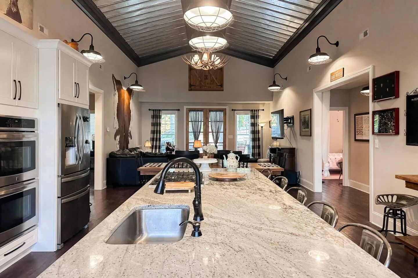Open concept kitchen and living area featuring a large granite island with an undermount sink, vaulted ceiling, and stainless steel appliances.