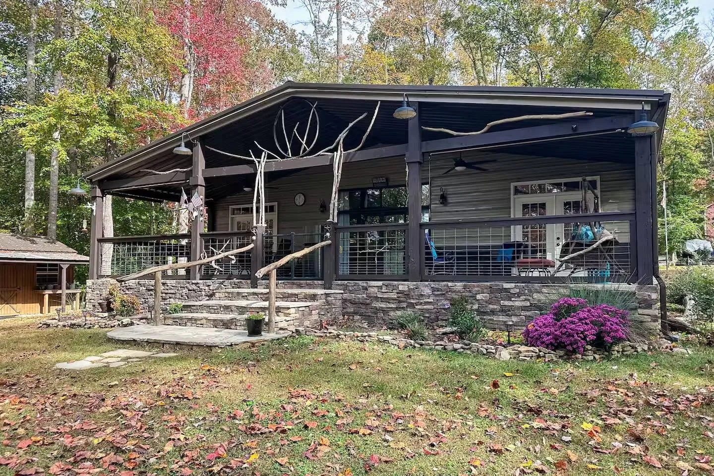 Exterior view of a cabin with a large covered front porch accented by rustic branch railings and stone-faced foundation.