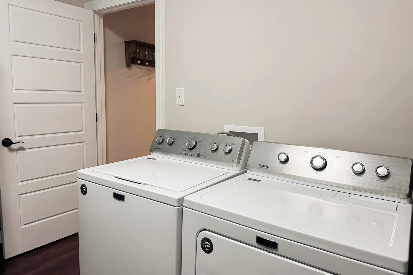 A white washer and dryer pair positioned along a neutral wall near an open white interior door.