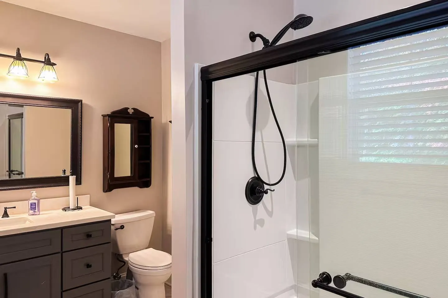 Bathroom with a vanity, toilet, and glass-enclosed shower with dark fixtures.