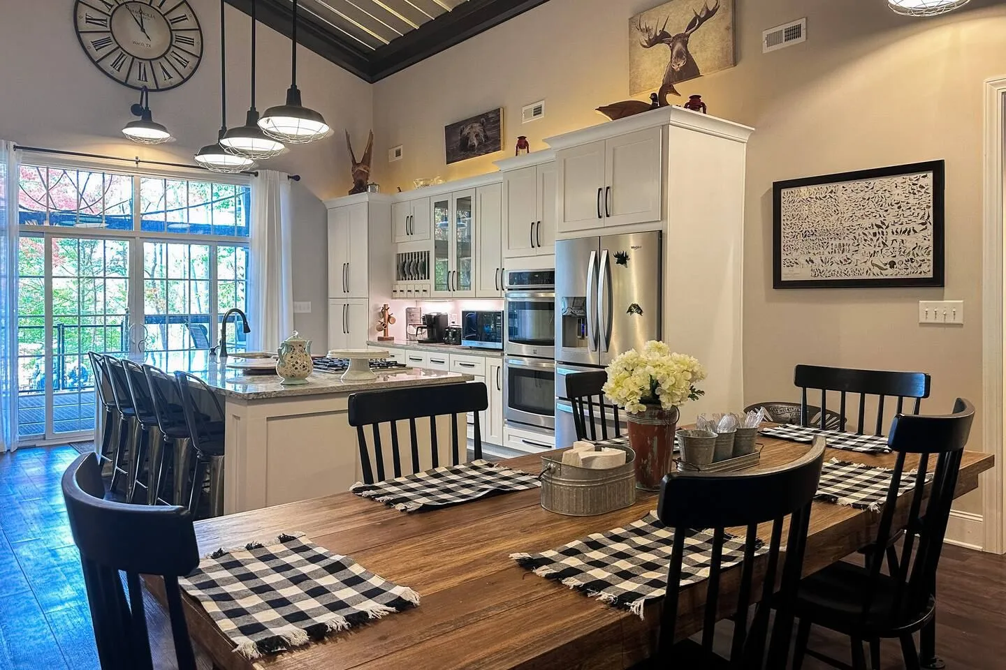 Open-concept dining area with a wooden table in the foreground looking toward a modern kitchen with white cabinets and a large island.