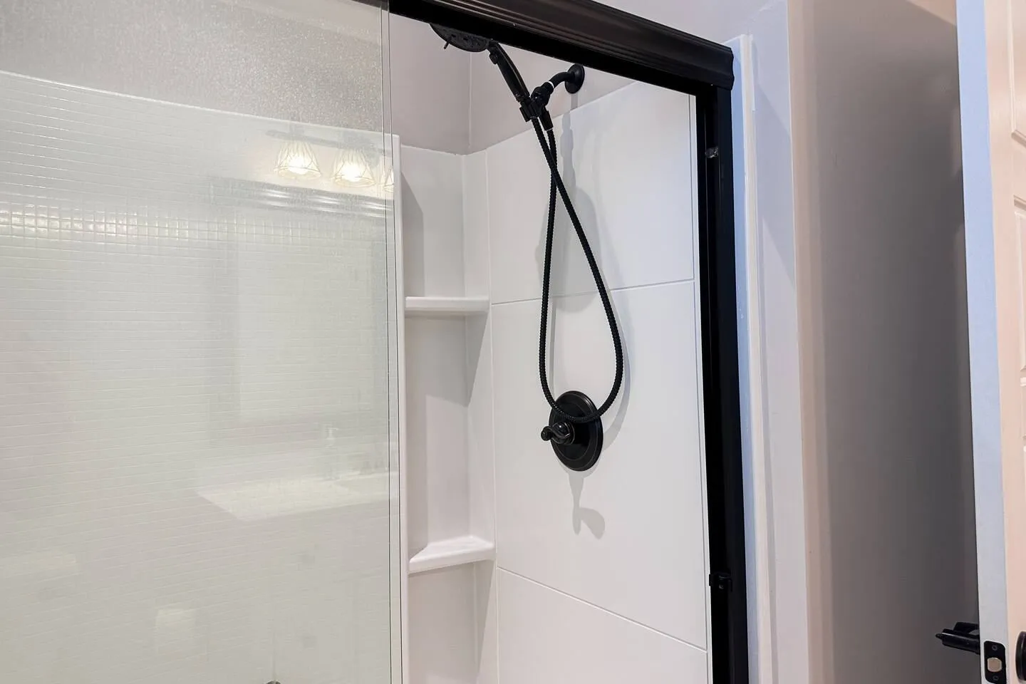 Close-up of a shower stall with white walls, black fixtures, and a glass door.