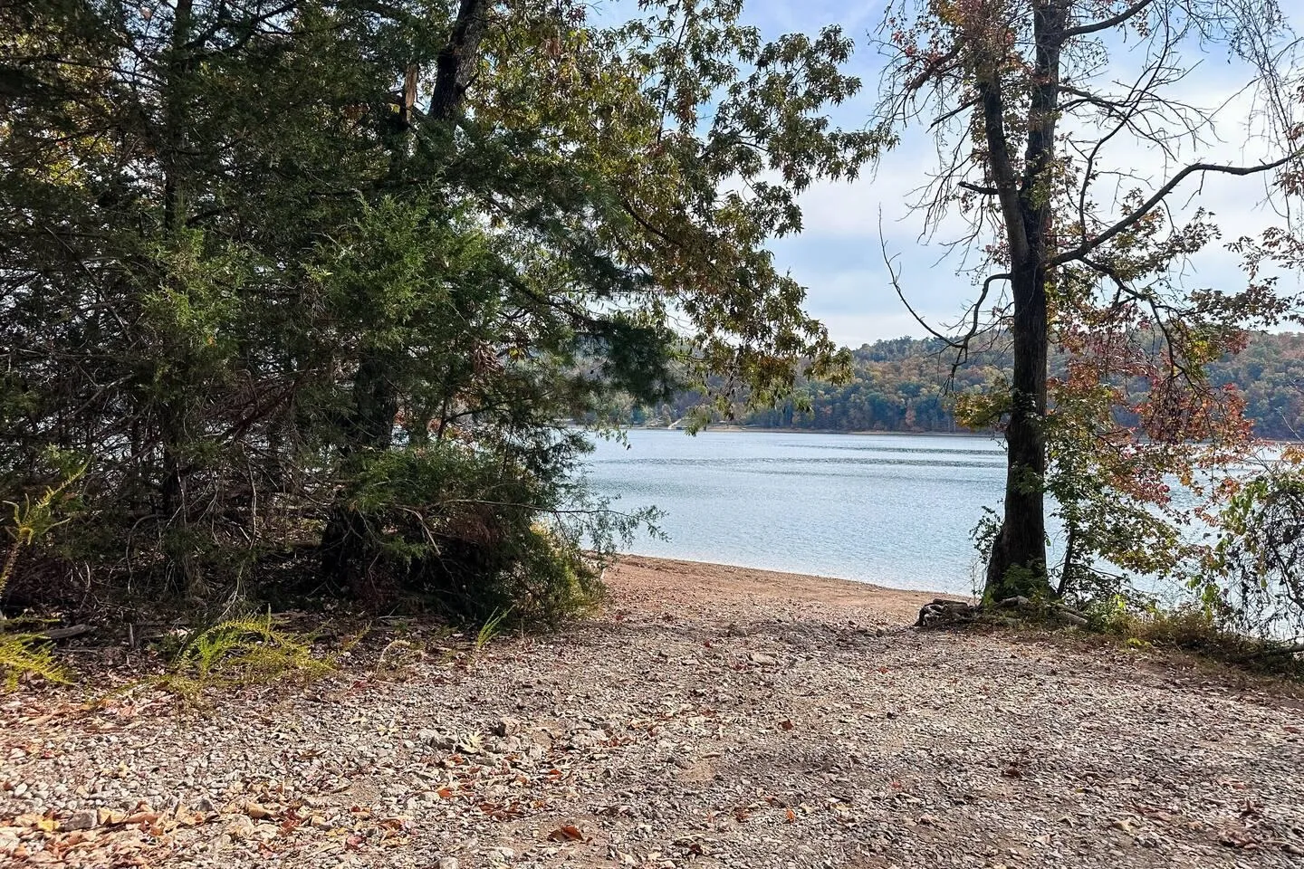 A gravel and dirt path leading down through trees to a sandy lake shore.