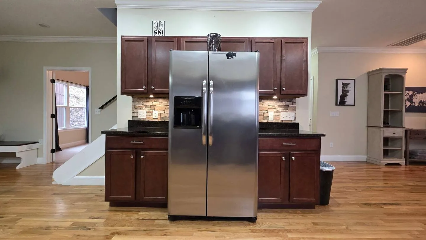 Stainless-steel side-by-side refrigerator flanked by dark wood kitchen cabinets with stone-look tile backsplashes.