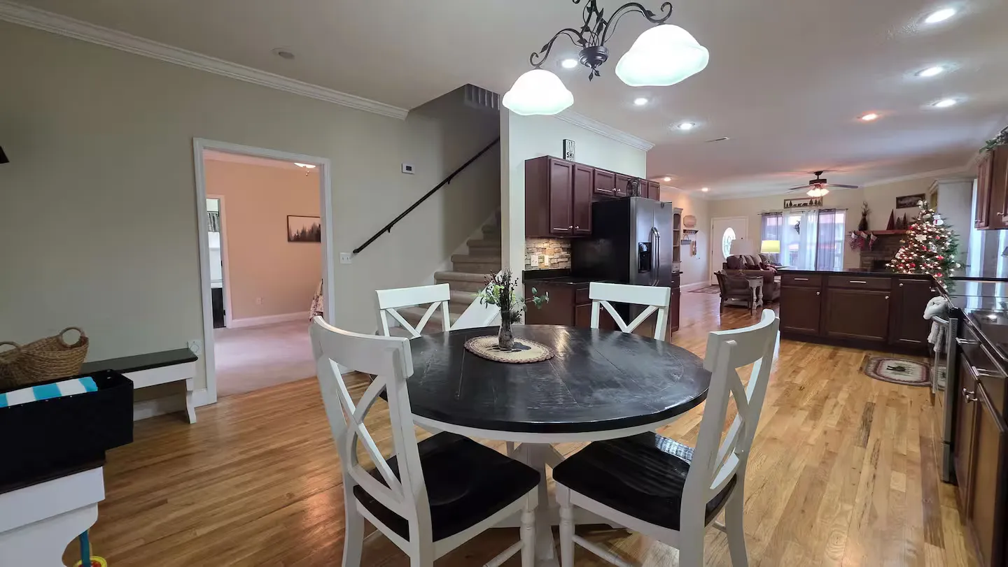 Open-concept dining and kitchen area featuring a round table with white chairs, wood flooring, and a view into the adjacent living space.