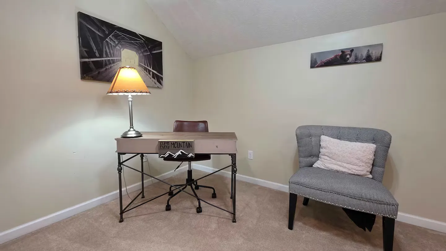 A carpeted workspace corner featuring a desk with a lamp and chair, alongside an upholstered accent armchair.