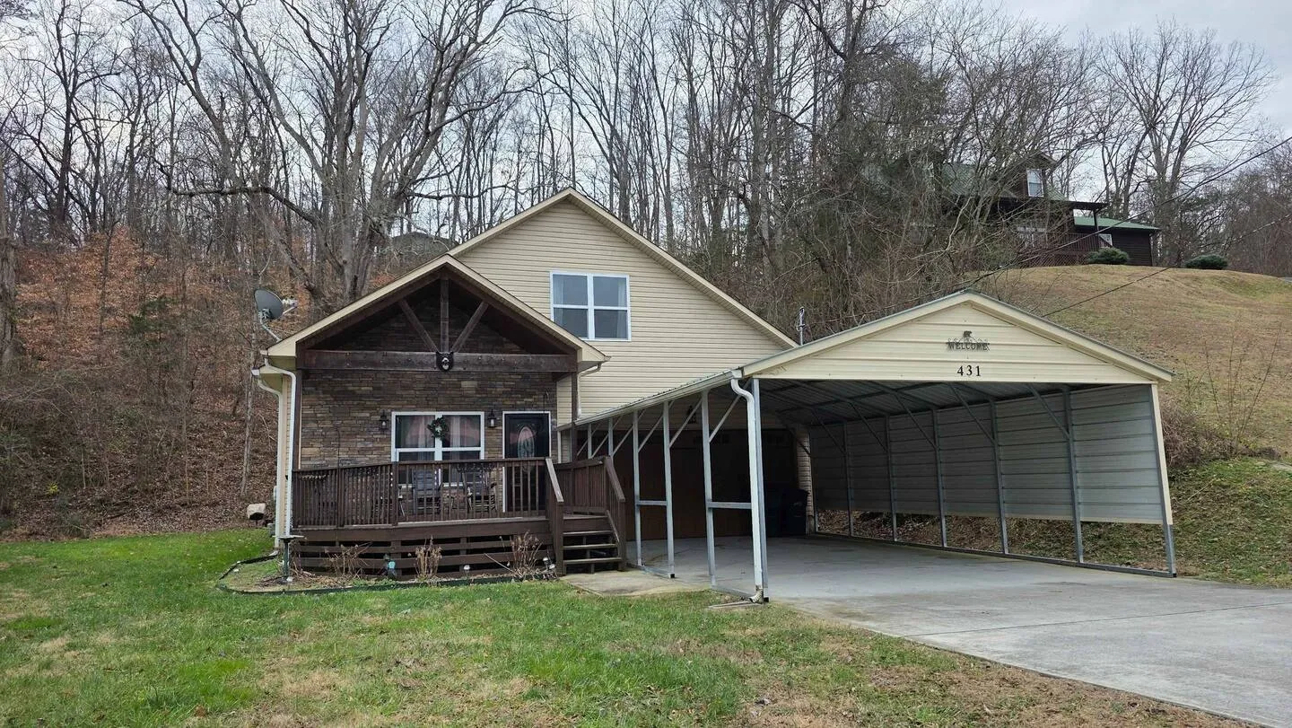 Exterior view of a home with siding, stone accents, a covered front porch, and an attached metal carport.
