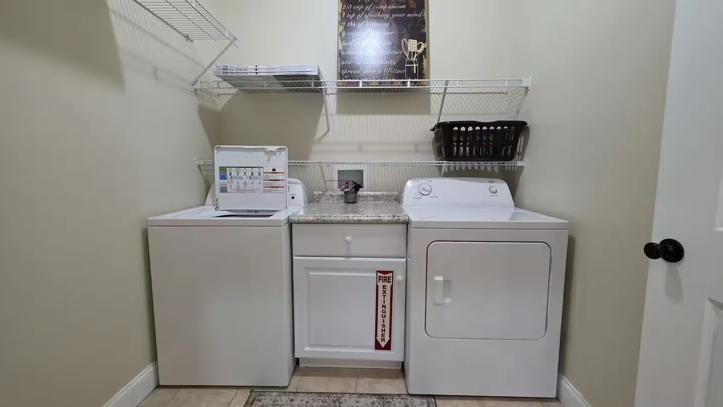 A laundry room with a white washing machine, white dryer, center countertop cabinet, and wire shelving above.