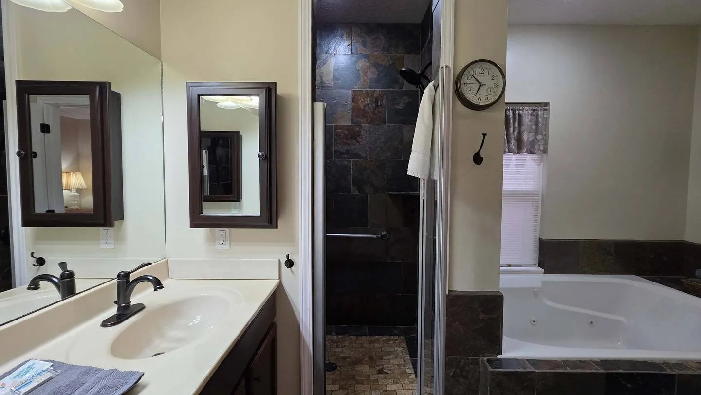 Bathroom showing a vanity sink, dark framed medicine cabinet, walk-in slate tile shower, and a corner jetted bathtub.