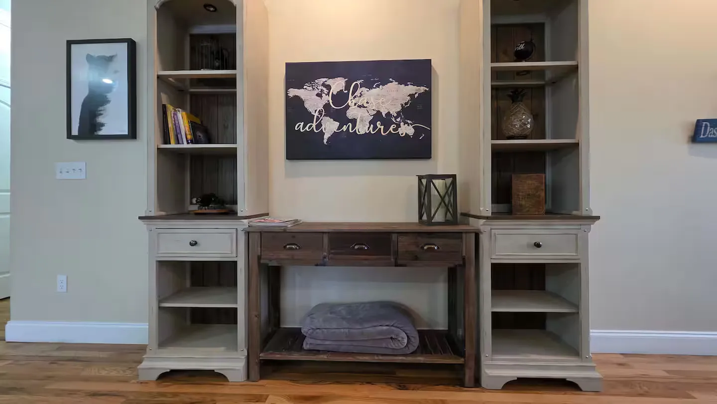 A wooden console table centered between two tall matching shelving units against a light-colored wall with hardwood flooring.