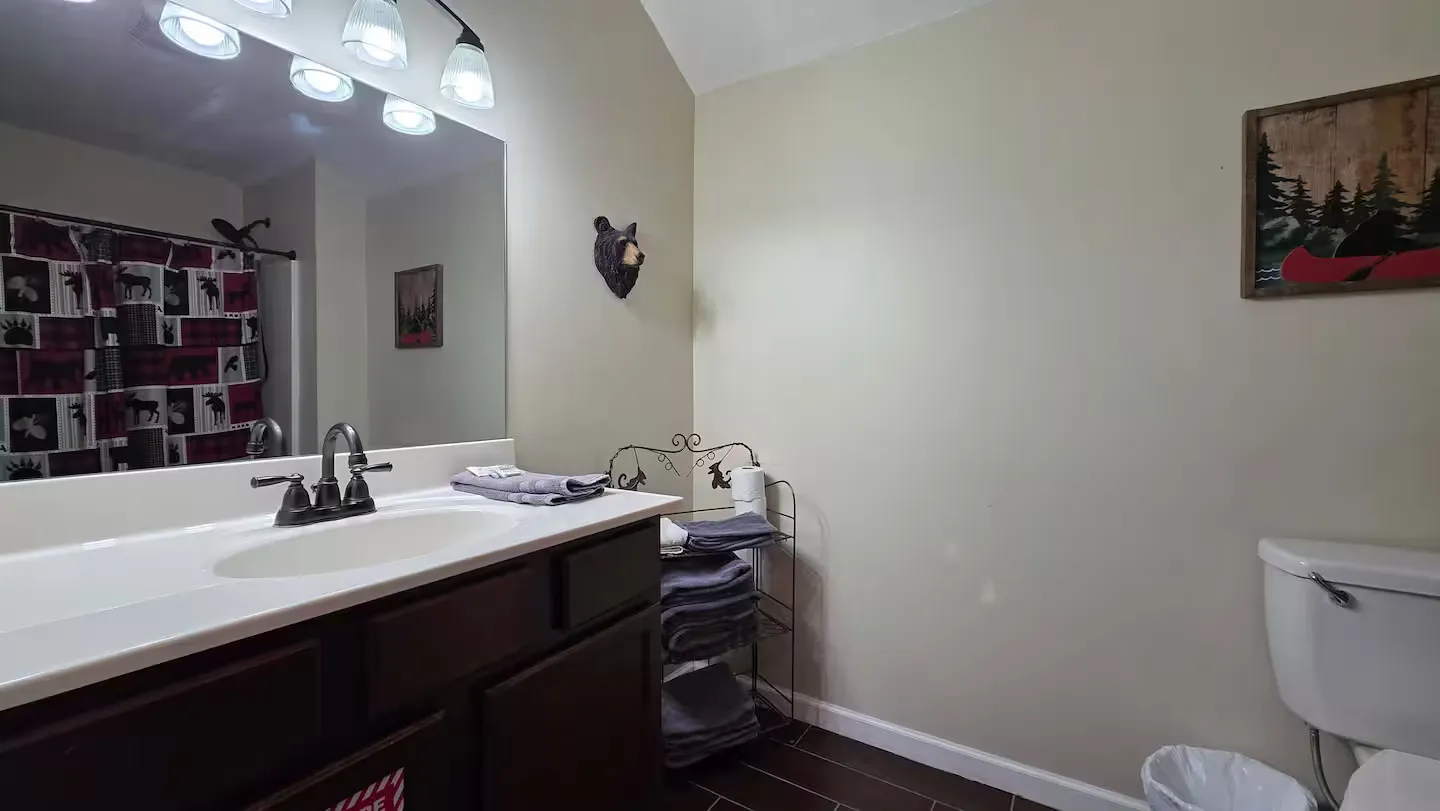 Bathroom with a dark vanity, white countertop, large mirror, small wire shelving unit with towels, and a toilet.