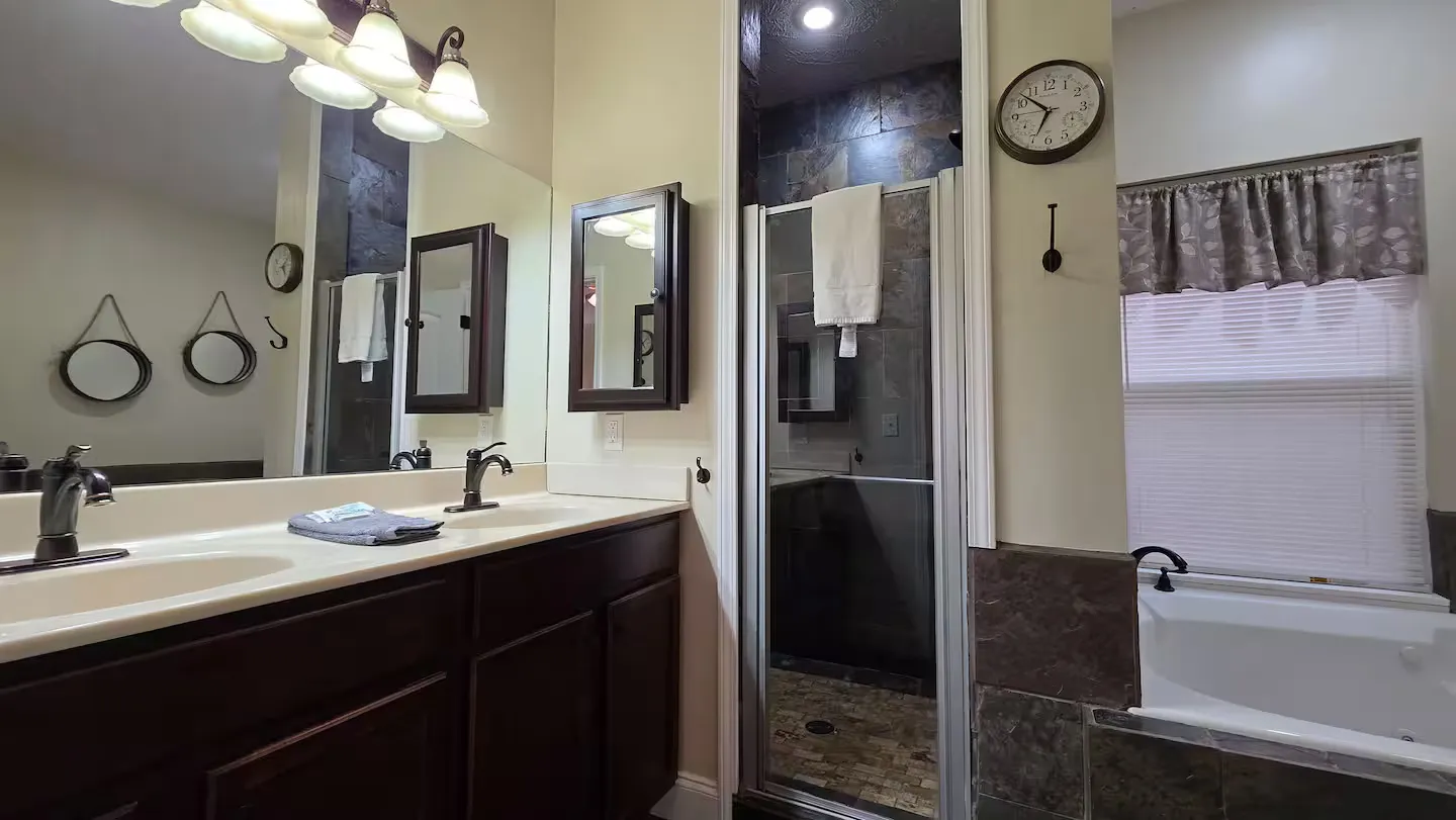 Bathroom with double sink vanity, large mirror, glass-door walk-in shower, and soaking tub by a window.