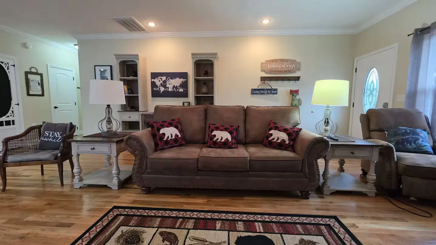 Living room featuring a brown sofa flanked by two end tables with lamps, a patterned rug, and rustic wall decor.