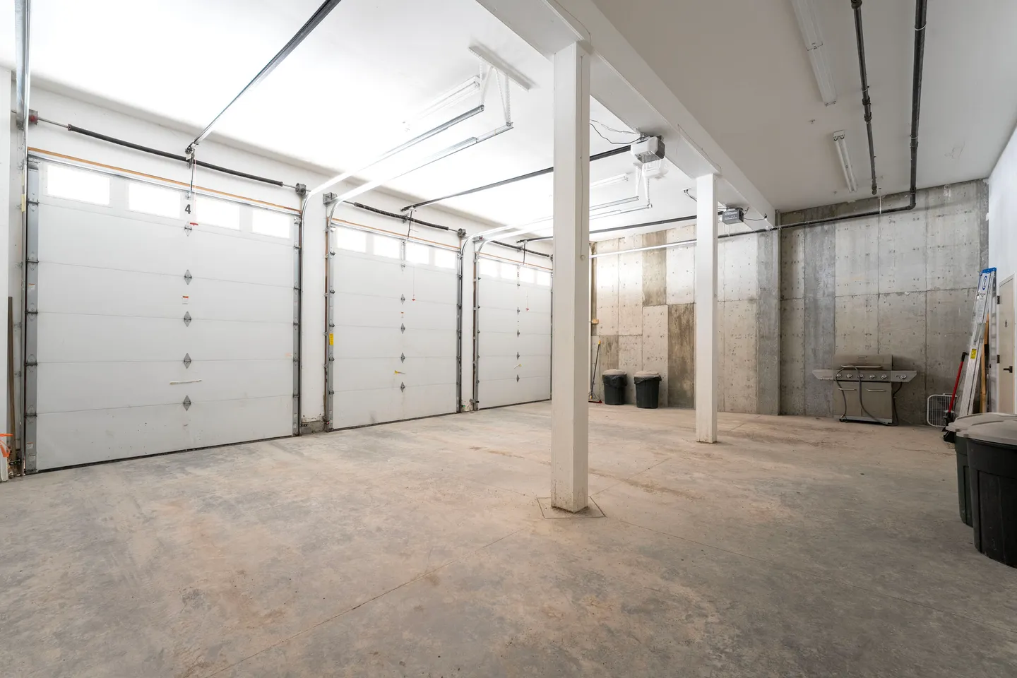 Spacious multi-car garage with concrete floor, white garage doors, and overhead lighting.