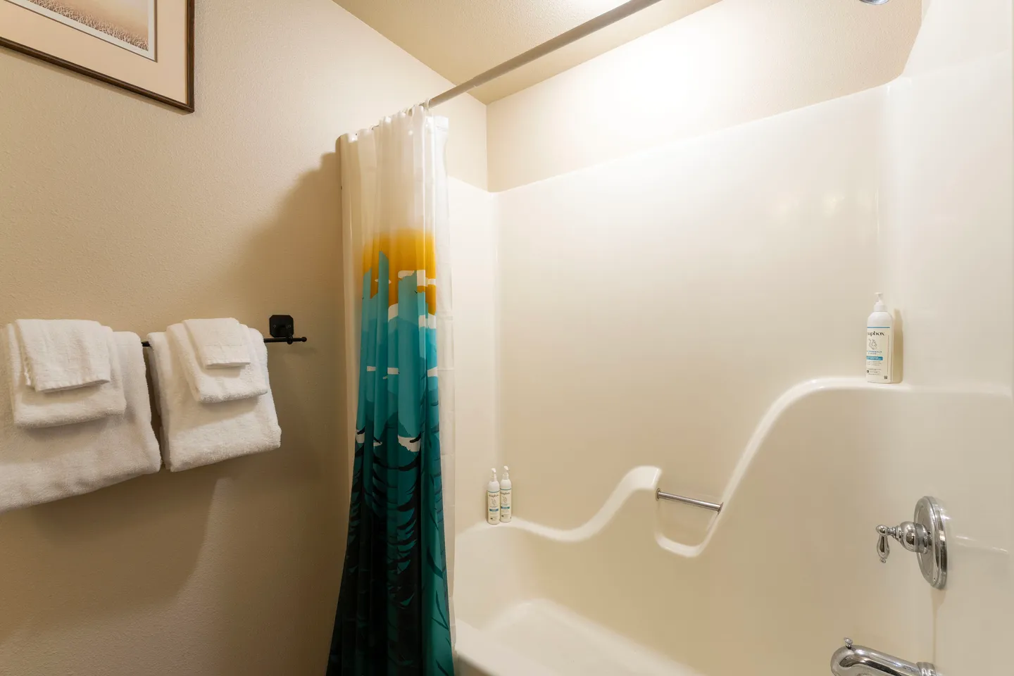 Bathroom shower and tub combination featuring a colorful printed shower curtain, molded white surround, and folded towels on a towel rack.