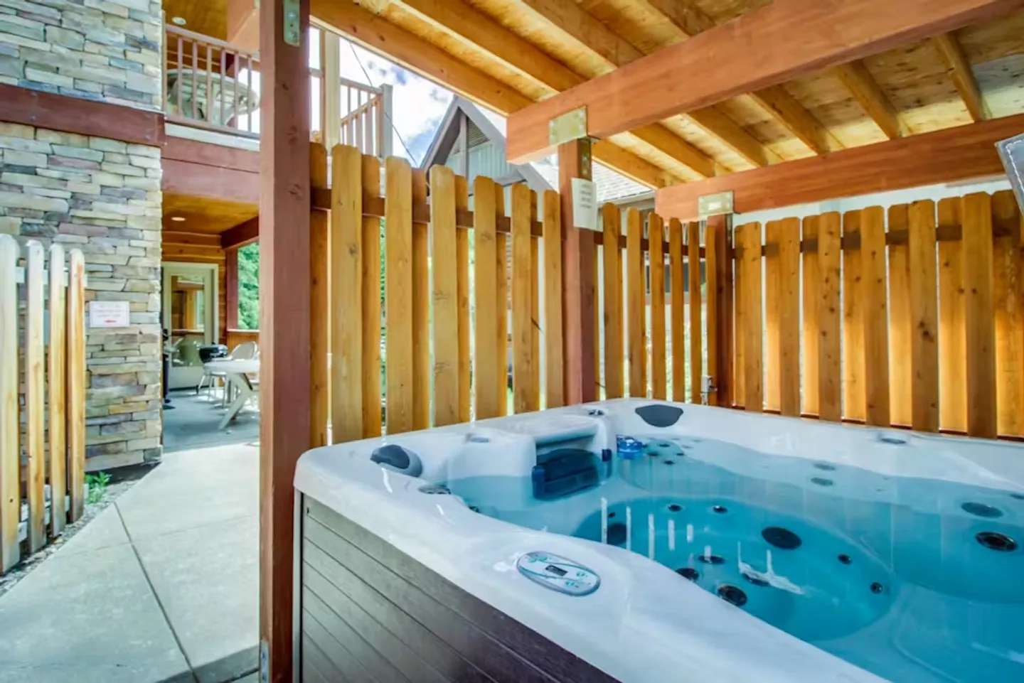 Outdoor hot tub filled with clear blue water under a wooden covered patio with a privacy fence.