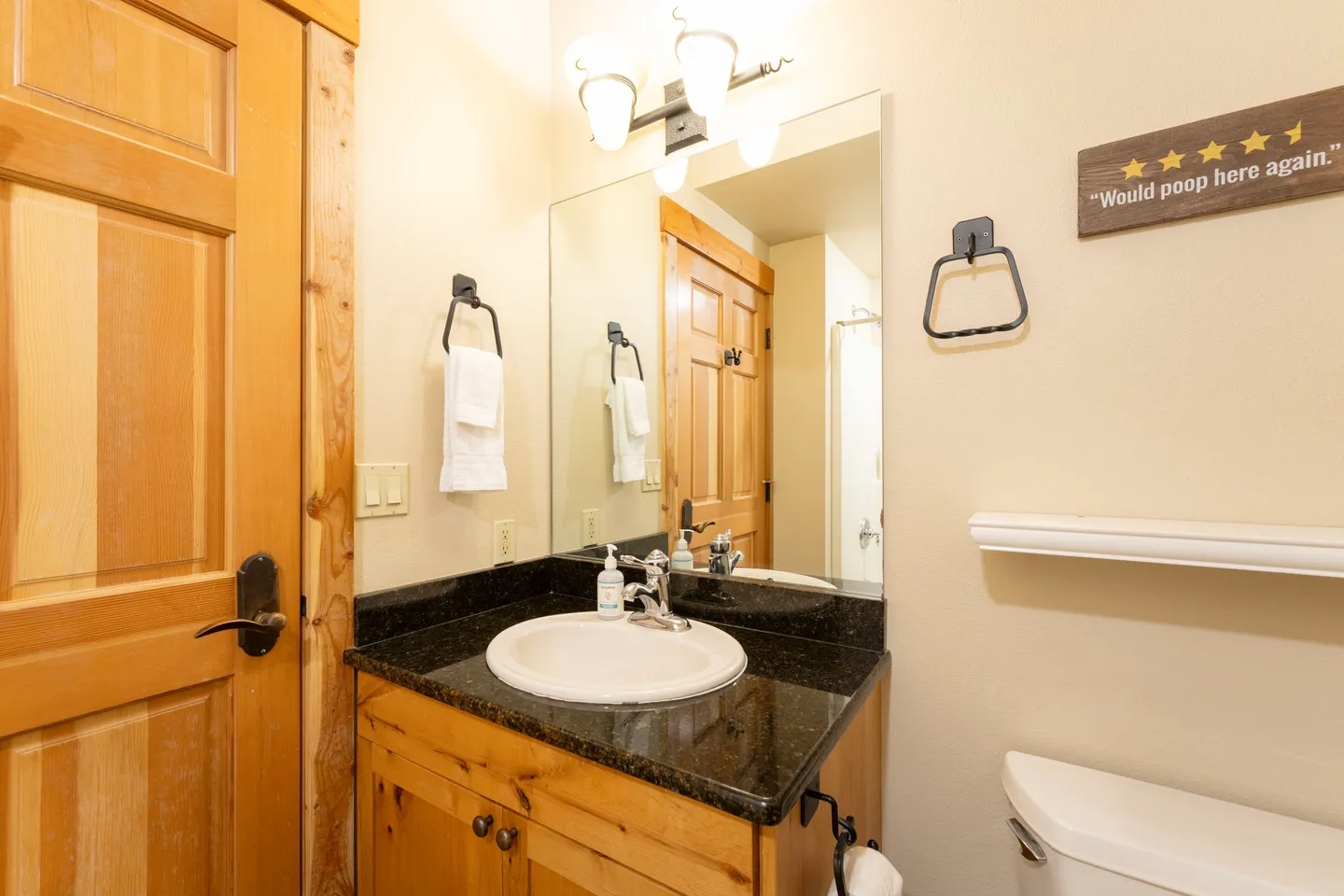 Bathroom with a rustic wooden vanity, dark speckled countertop, mirror, and toilet.