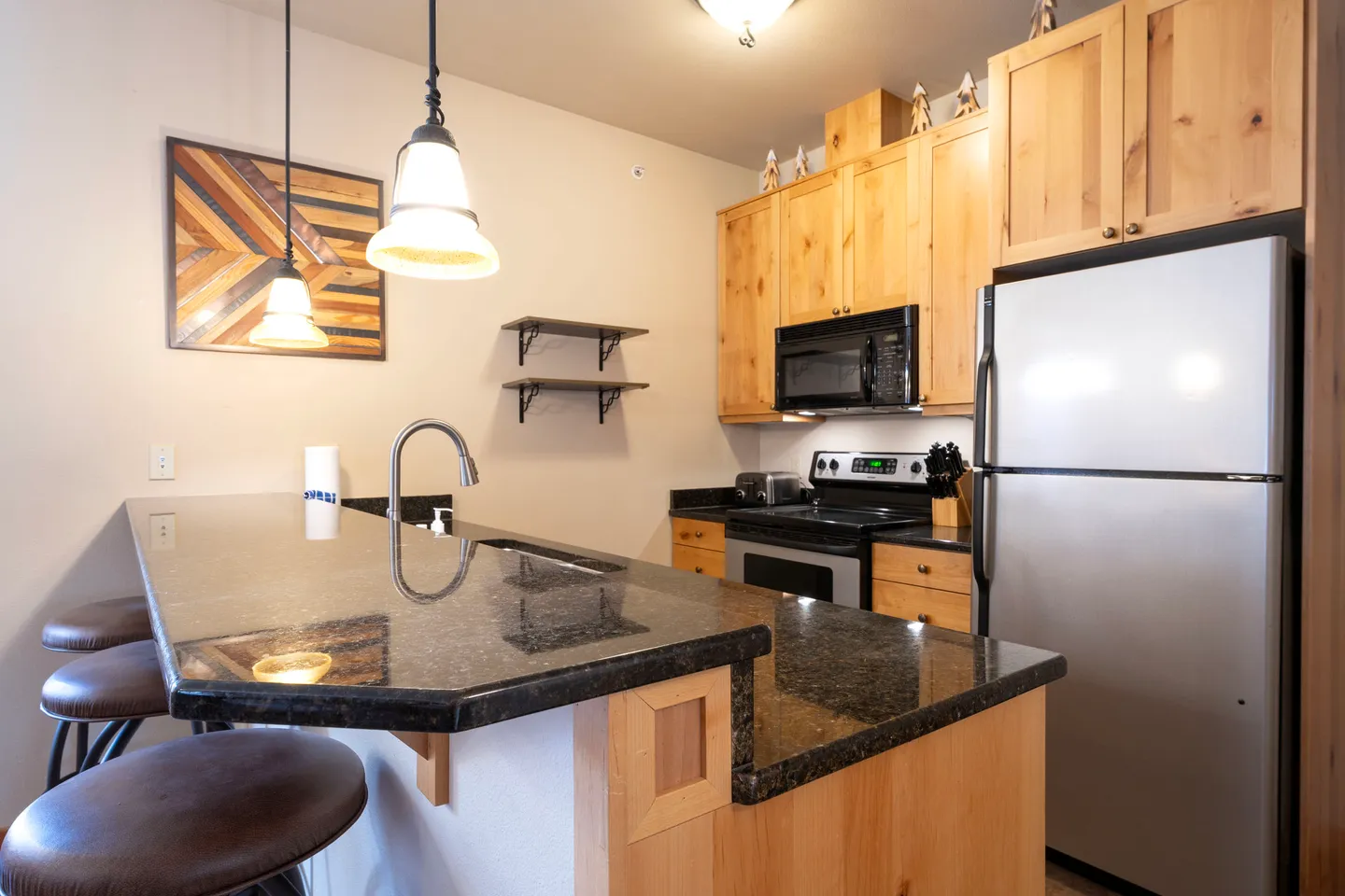 Kitchen with dark polished countertops, light wood cabinetry, stainless steel appliances, and a breakfast bar with stools.