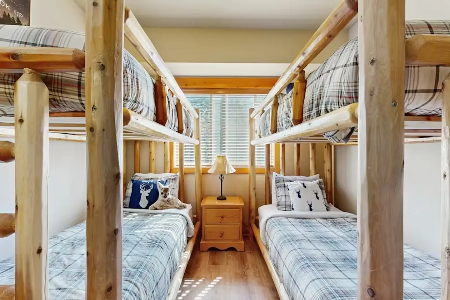 A bedroom with two sets of log bunk beds flanking a window and a small wooden nightstand.