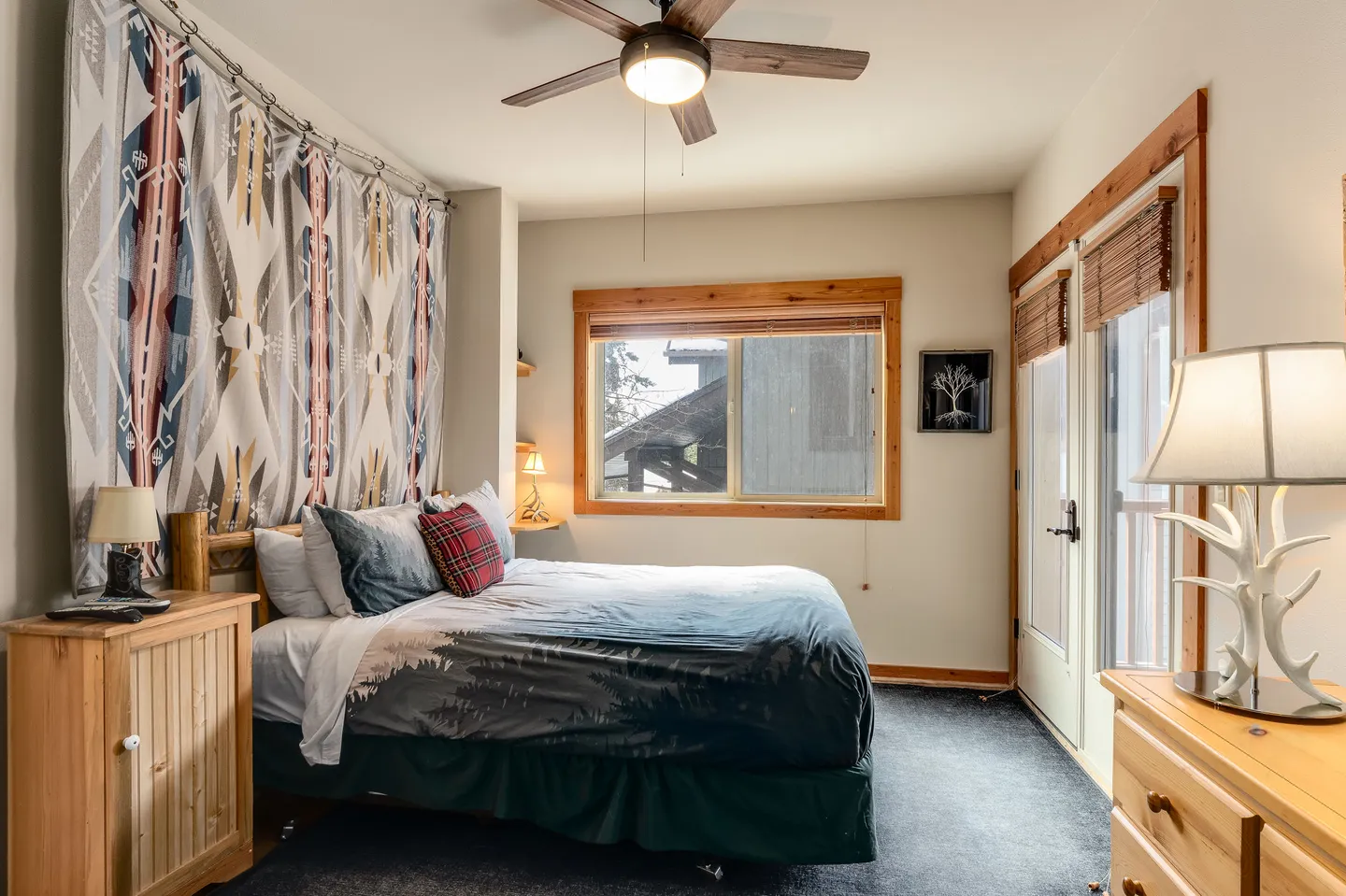 Bedroom with a patterned wall tapestry, carpeted floor, ceiling fan, wooden dressers, and a glass door leading outside.