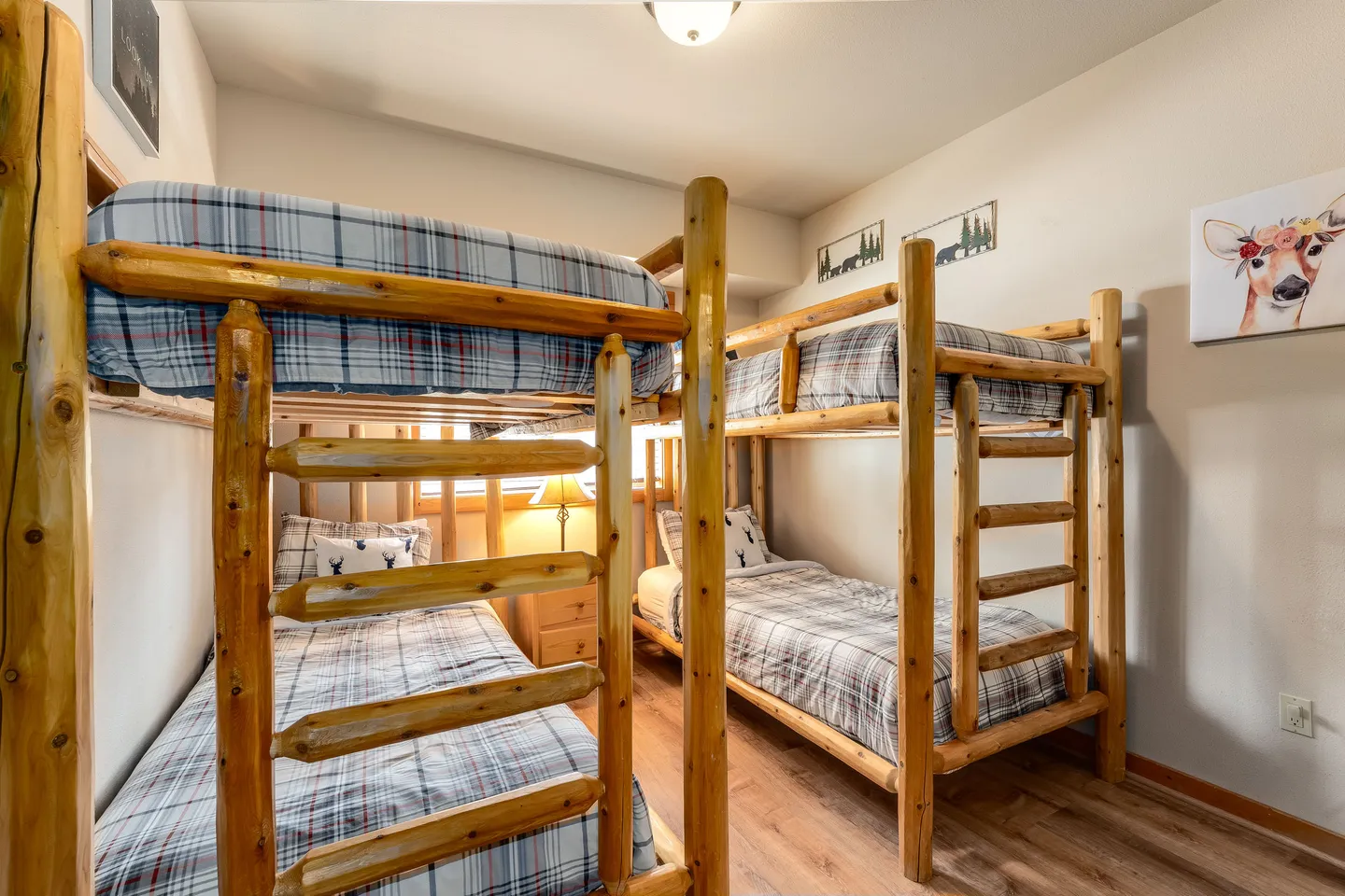 Bedroom featuring two sets of rustic log-frame bunk beds with plaid bedding and wood-look flooring.