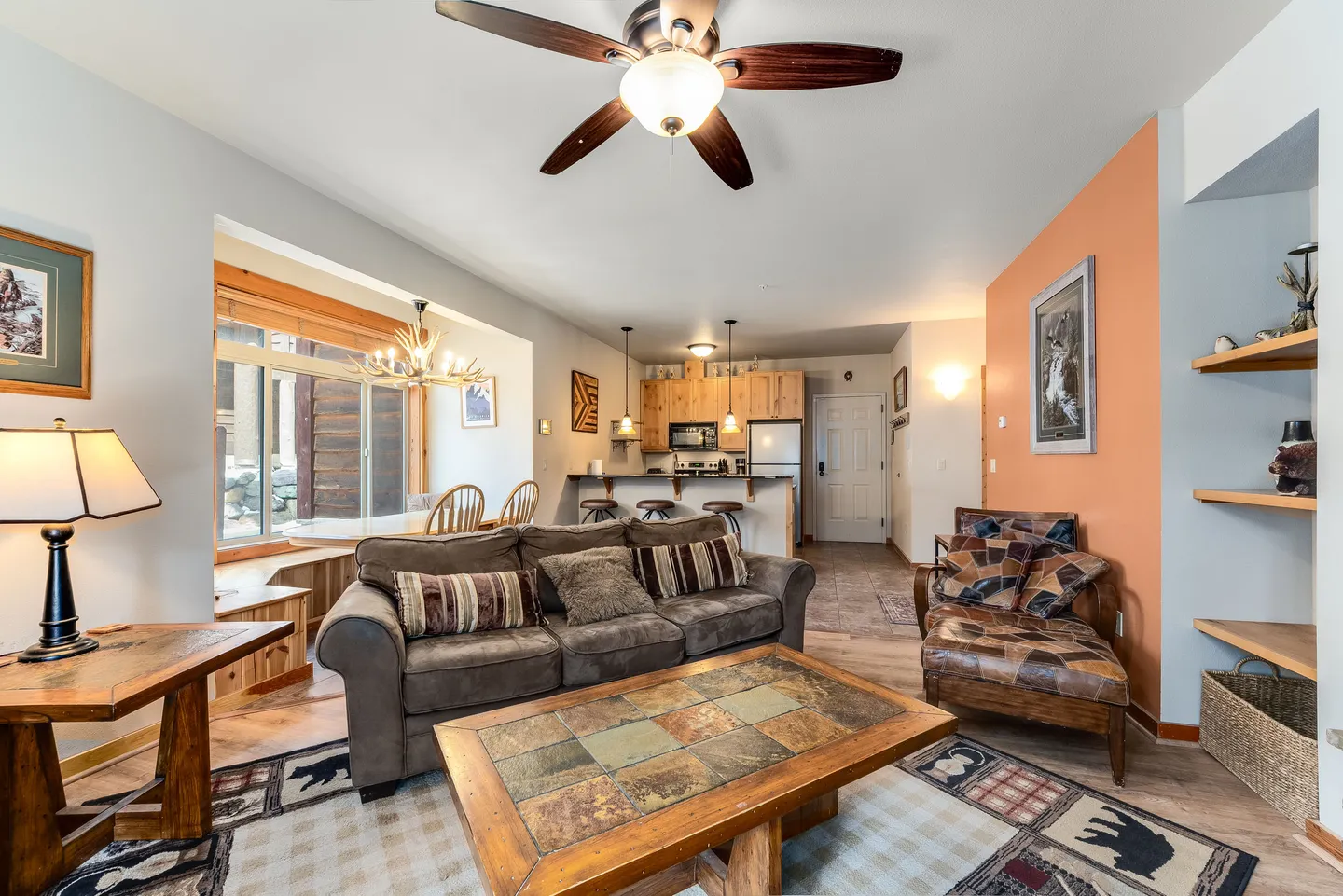Open-concept living room with a brown sofa, tile-top coffee table, ceiling fan, and view into the kitchen and dining area.