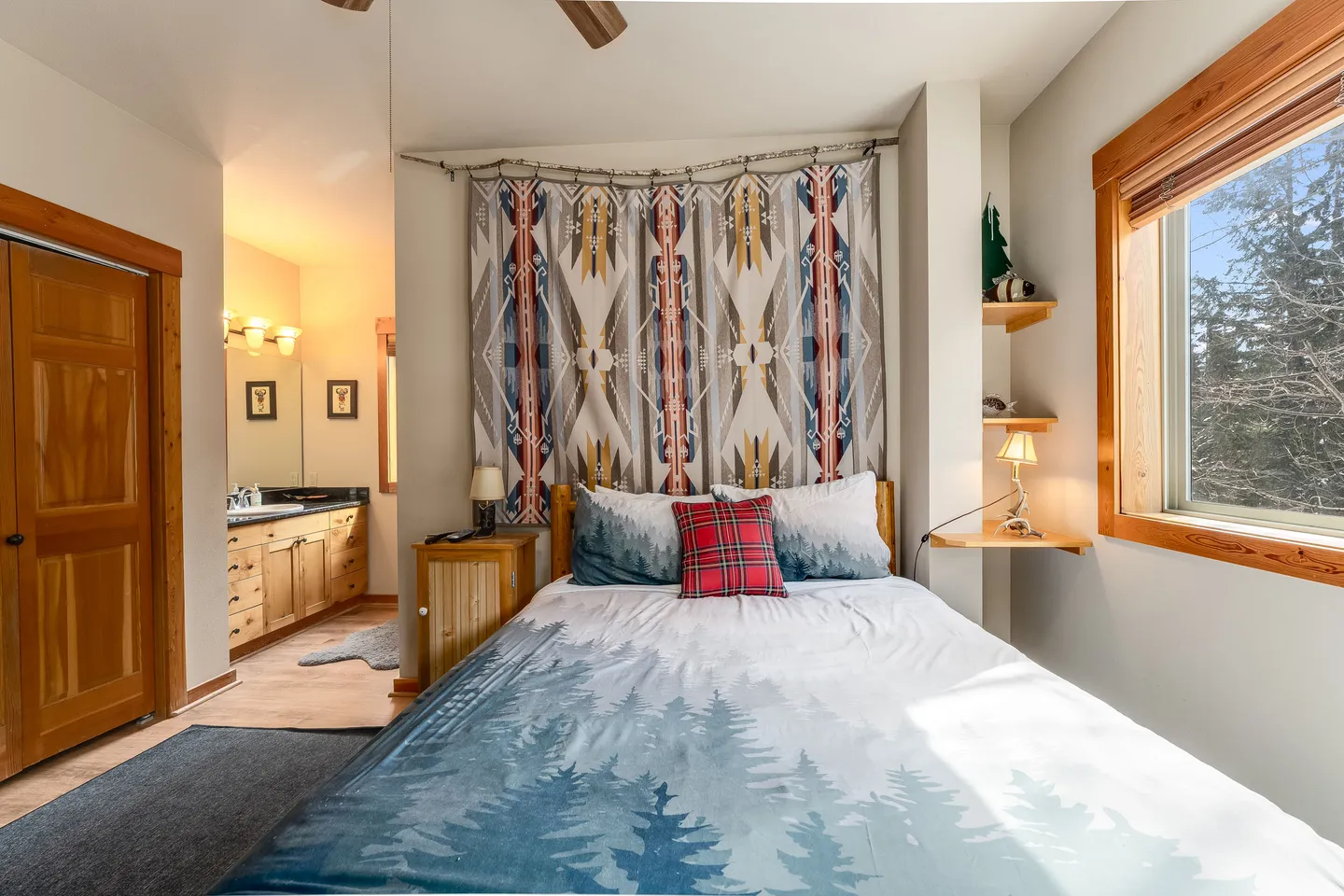 Bedroom featuring a patterned tapestry behind the bed, a window looking outside, and a view into an attached bathroom.