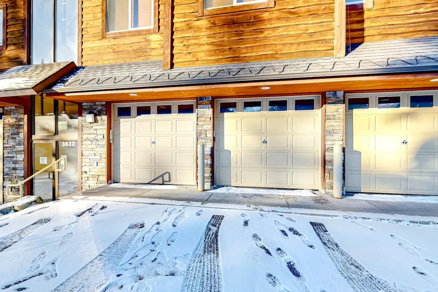 Exterior view of three garage doors beneath a log-sided building with snow covering the driveway.