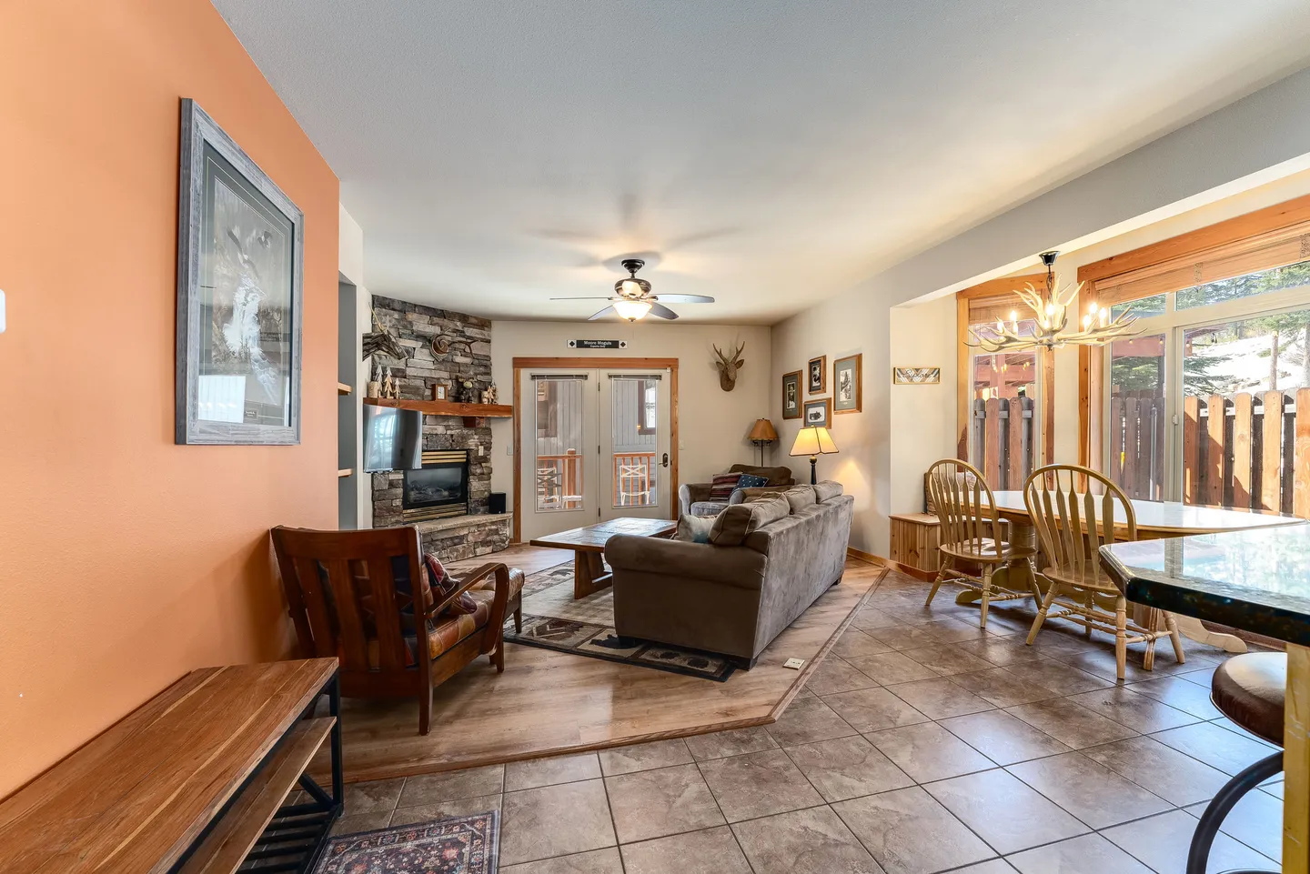 Open living and dining area featuring a stone corner fireplace, sofa seating, tiled dining space, and glass doors leading outdoors.