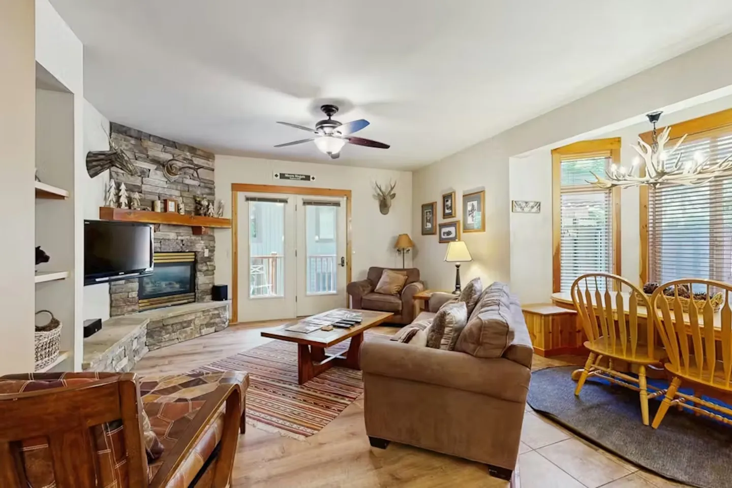 Living and dining area featuring a stone corner fireplace, sofa, coffee table, and adjacent wooden dining table with chairs.
