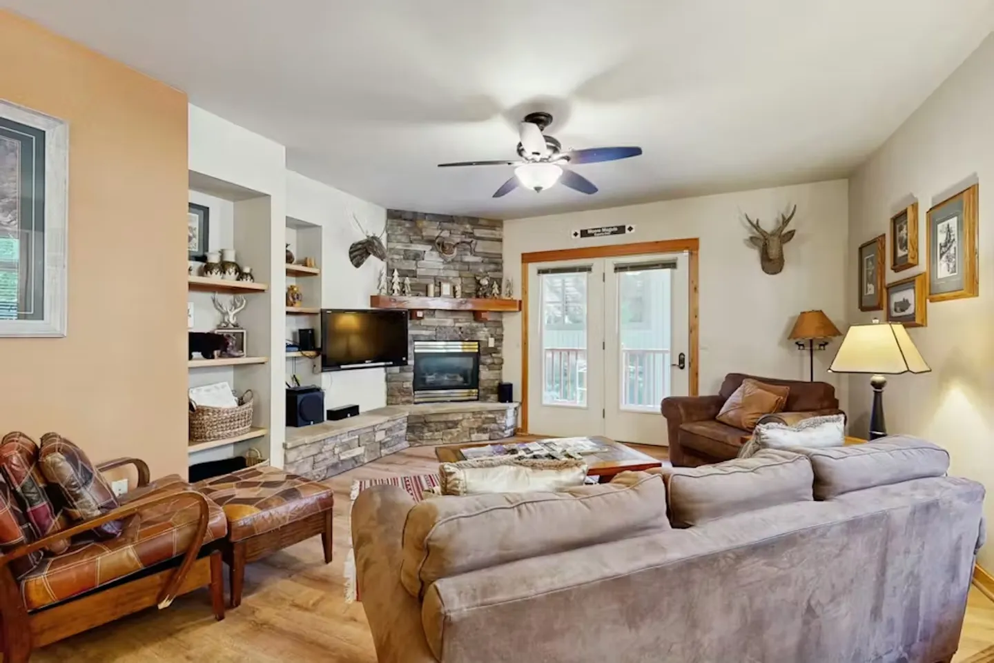 Living room with a stone corner fireplace, mounted television, ceiling fan, sofa, and leather armchairs.