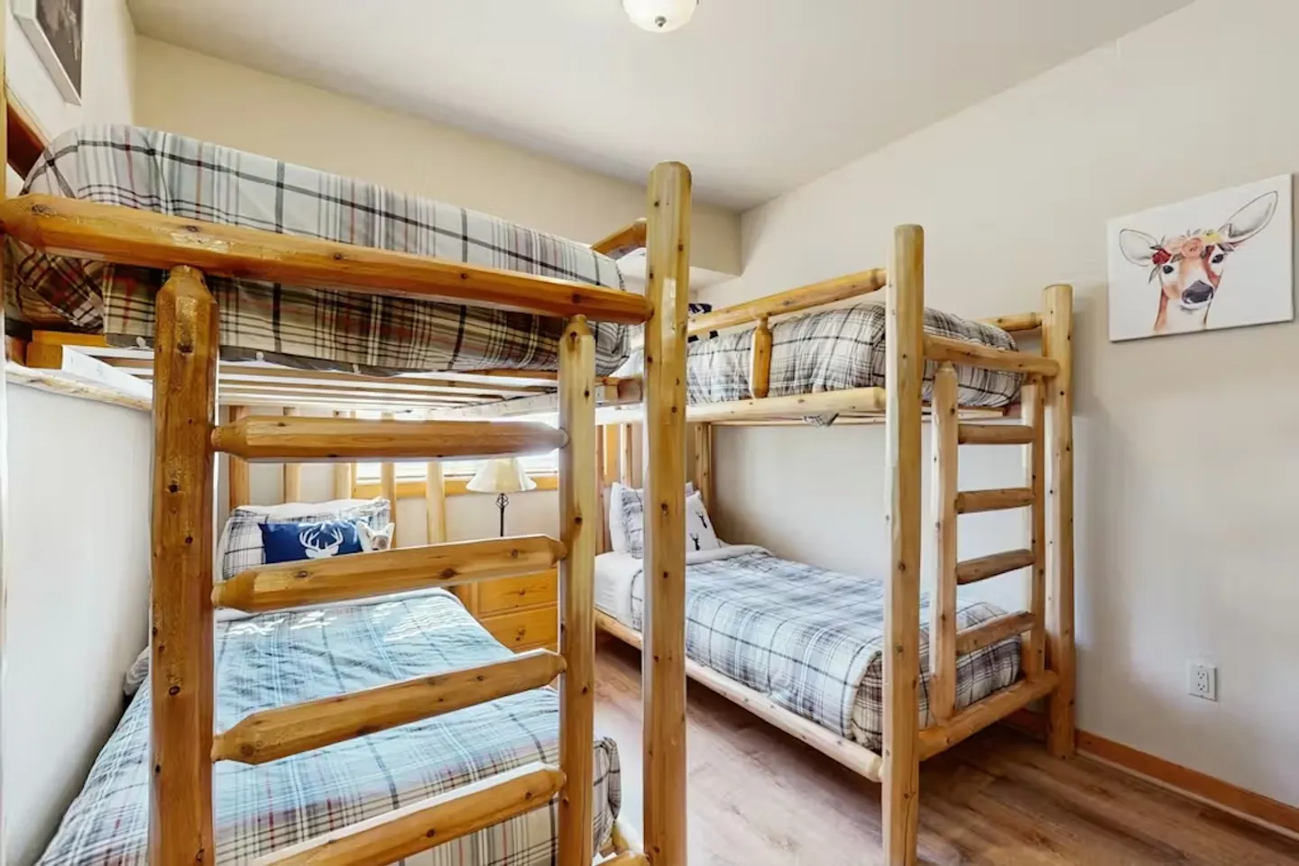 Bedroom featuring two sets of rustic log-style bunk beds with plaid bedding and light wood-look flooring.