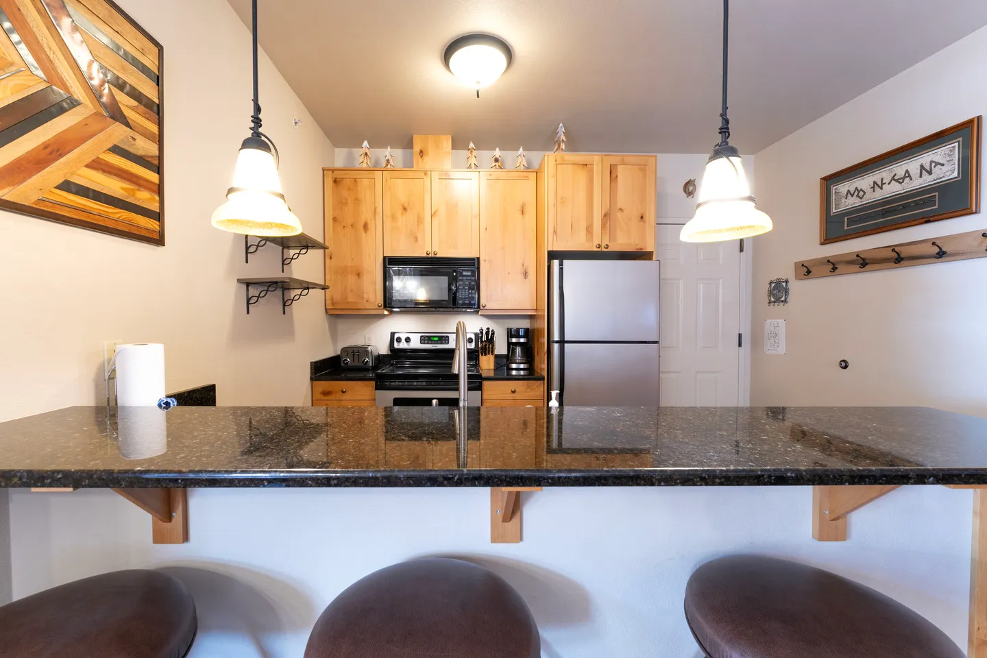 Kitchen counter and breakfast bar with dark countertops, wooden cabinets, stainless steel refrigerator, and pendant lights.