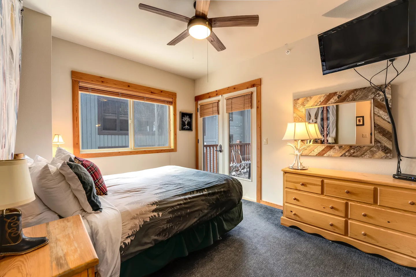 Bedroom featuring a made bed, wood dresser, wall-mounted television, ceiling fan, and glass doors leading outside.