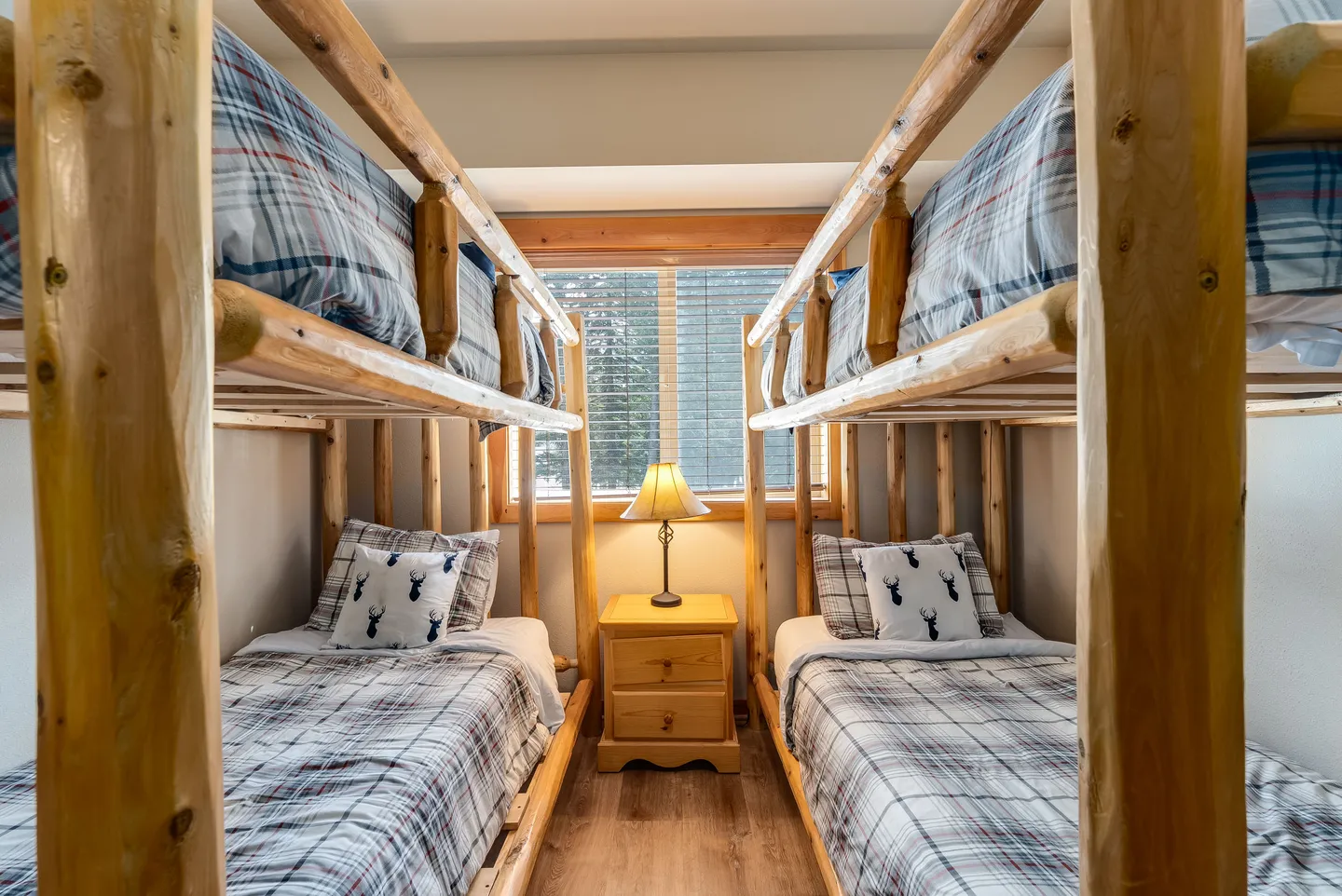Bunk room featuring two sets of rustic log bunk beds flanking a window with a nightstand and lamp.