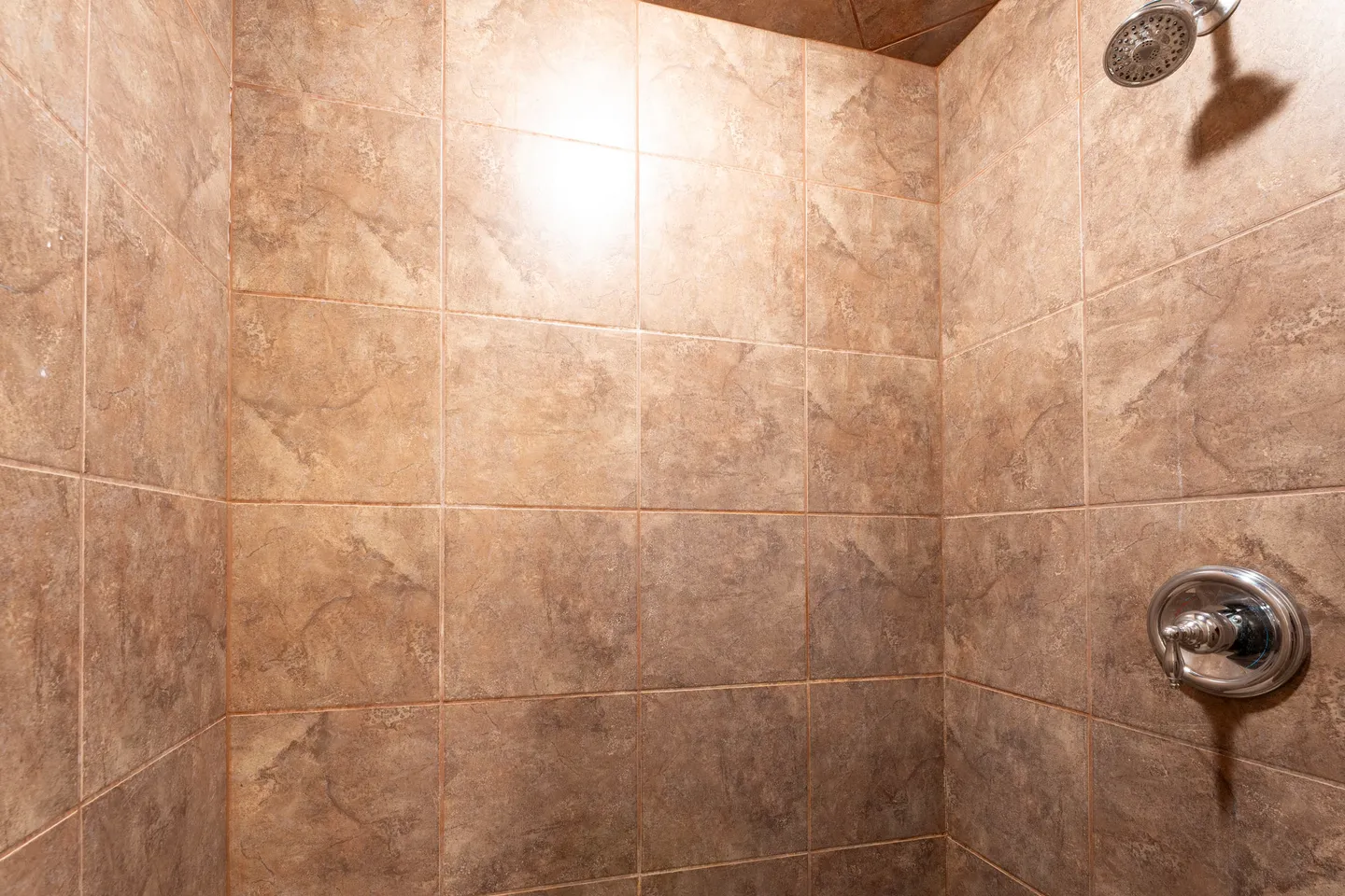 Tiled shower enclosure featuring brown earth-toned square tiles and chrome fixtures.