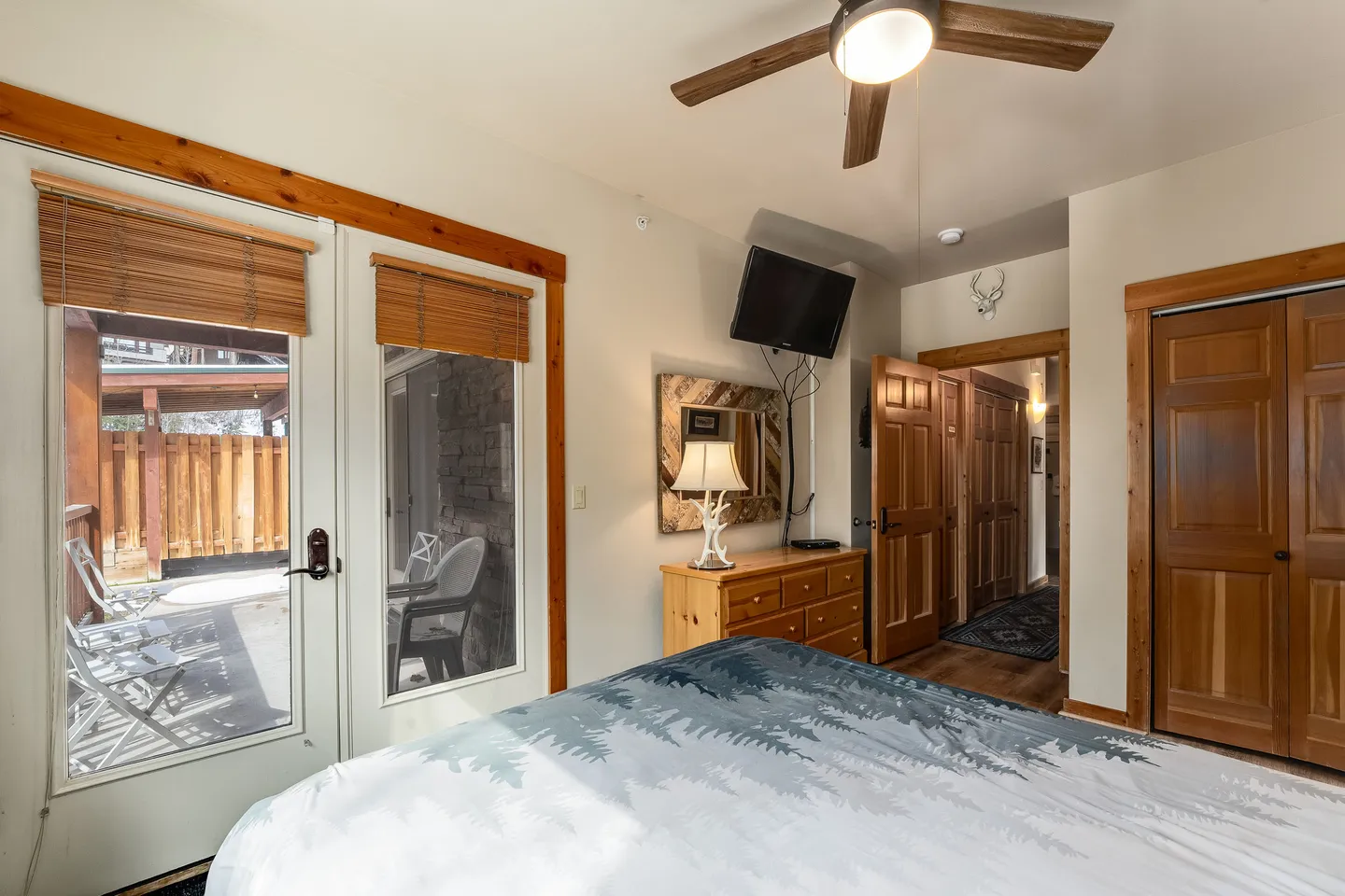 Bedroom with patterned bedding, a ceiling fan, a dresser with a mounted TV, and glass doors opening to a patio.