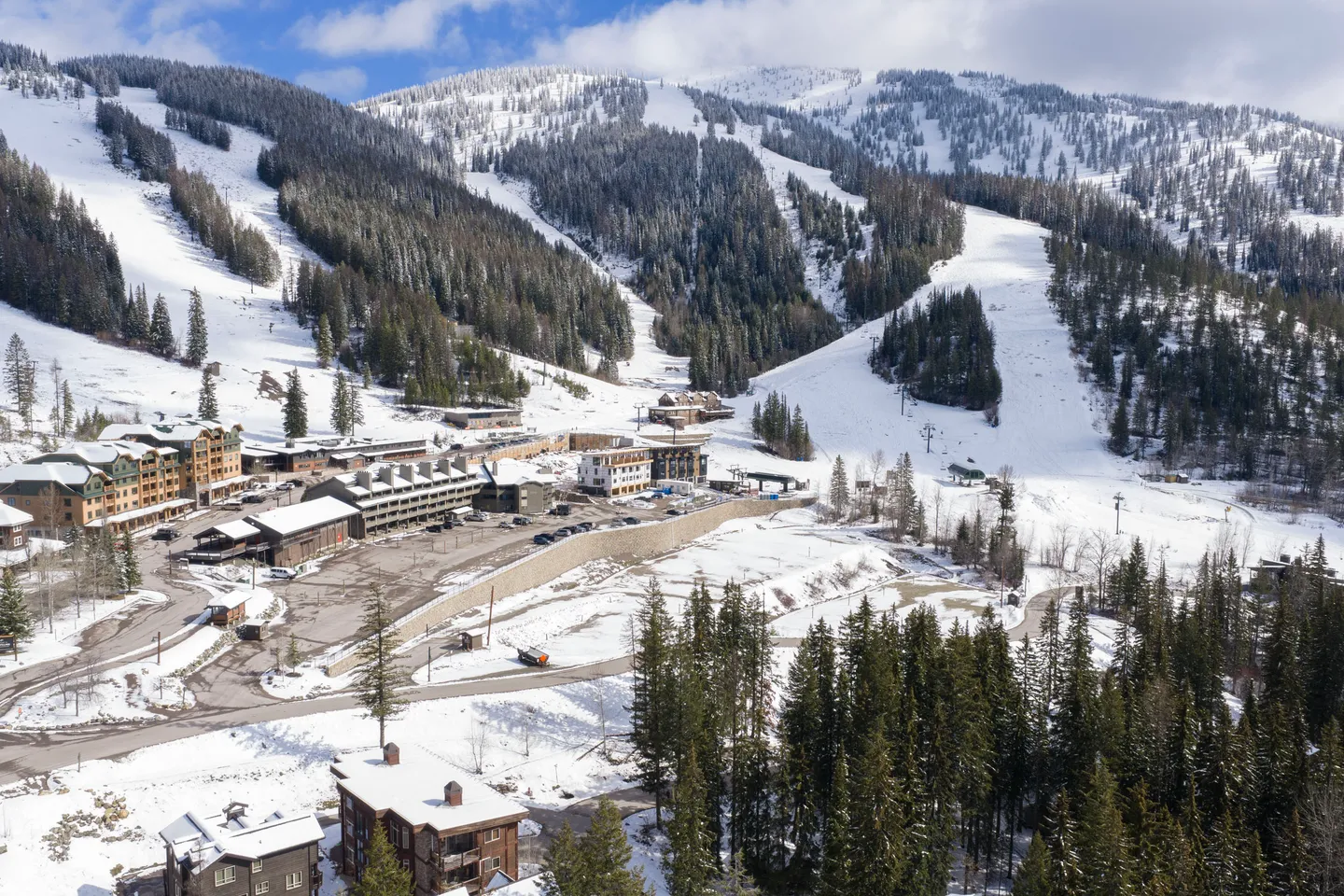 Aerial view of a ski resort village with lodges and parking lots at the base of snow-covered mountain ski runs.