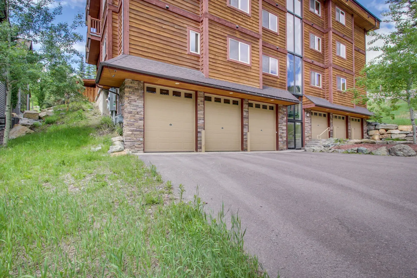 Exterior view of a multi-story wood-sided building with multiple ground-level garage bays and an asphalt driveway.