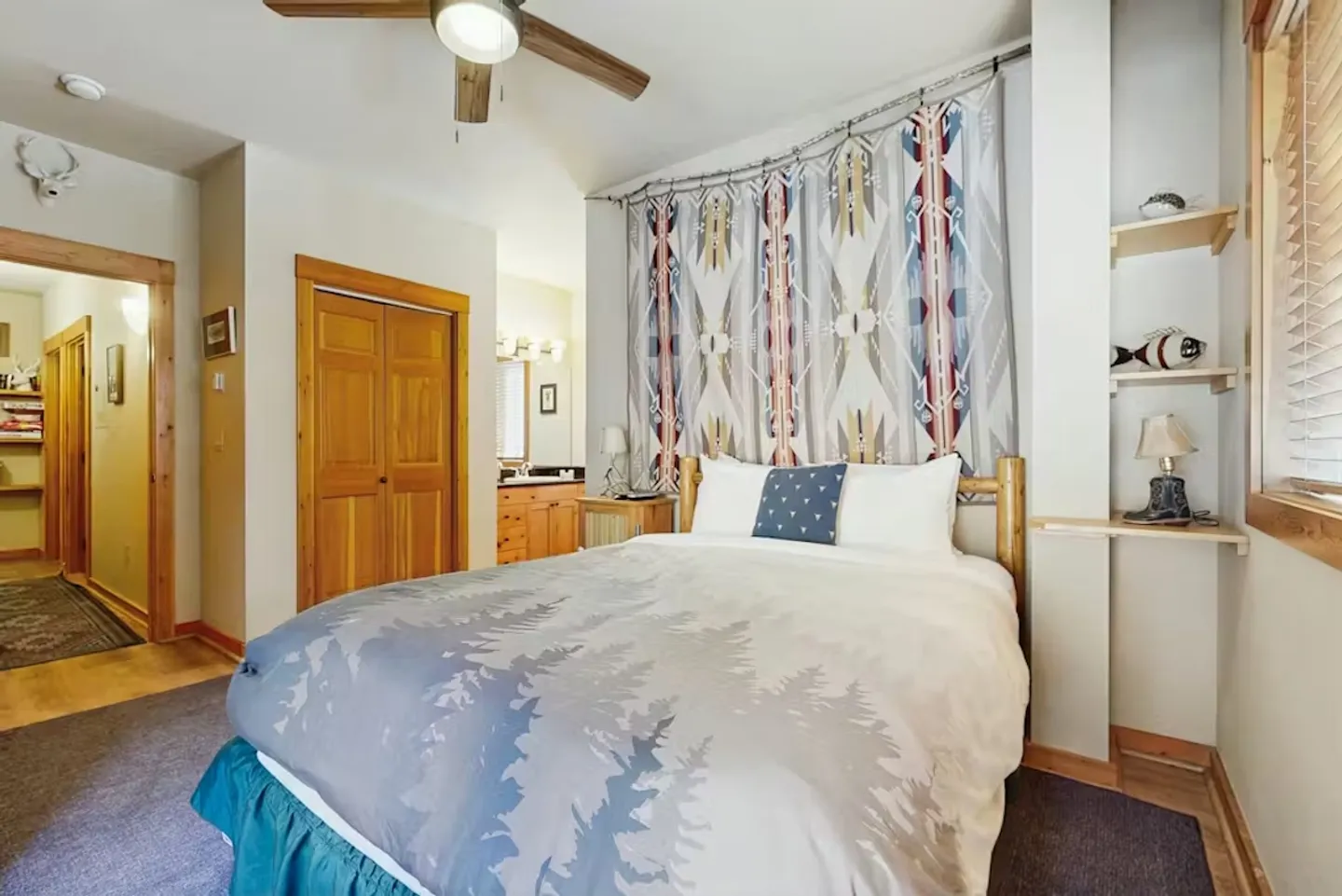 Bedroom with a wooden log-style bed, printed blanket, hanging tapestry, and an adjoining bathroom.