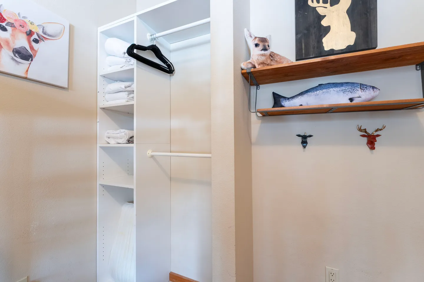 Open closet with white shelving and hanging rods next to wall-mounted shelves decorated with animal-themed items.